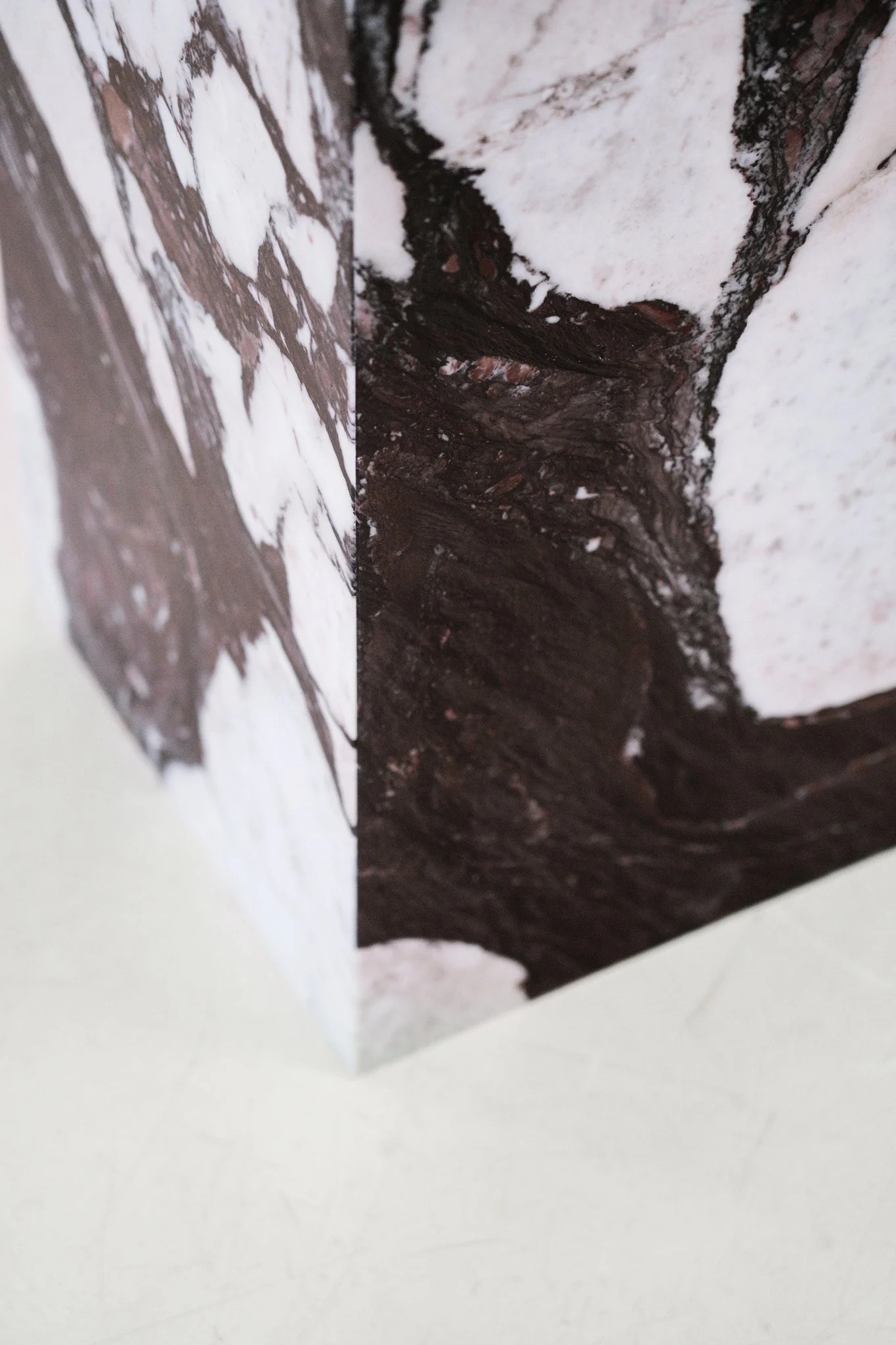 En pedestal med marmormønster på overfladen, placeret på en hvid flade med grå baggrund. Kube piedestal i den smukke high-end marmor Calacatta Viola.