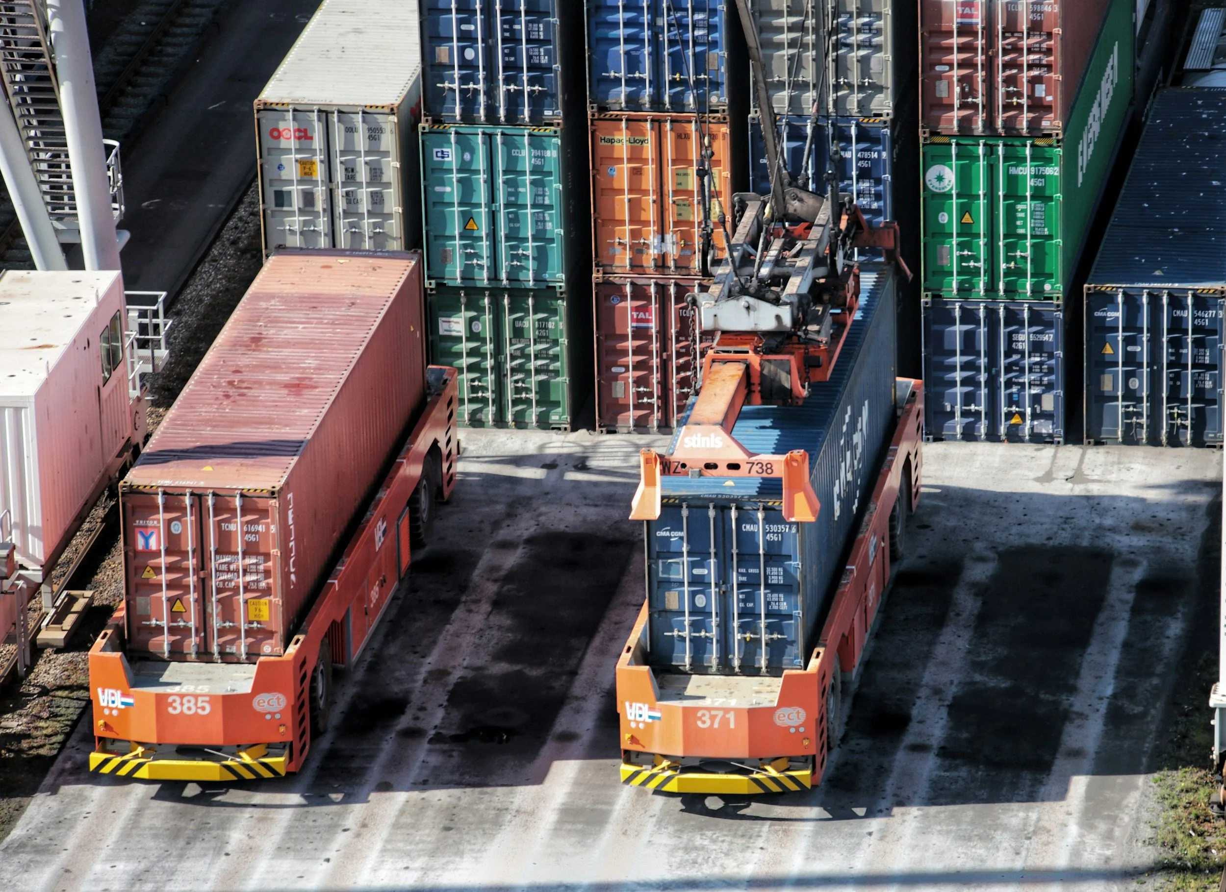 Two orange rail yard vehicles moving stacks of shipping containers on railroad tracks.