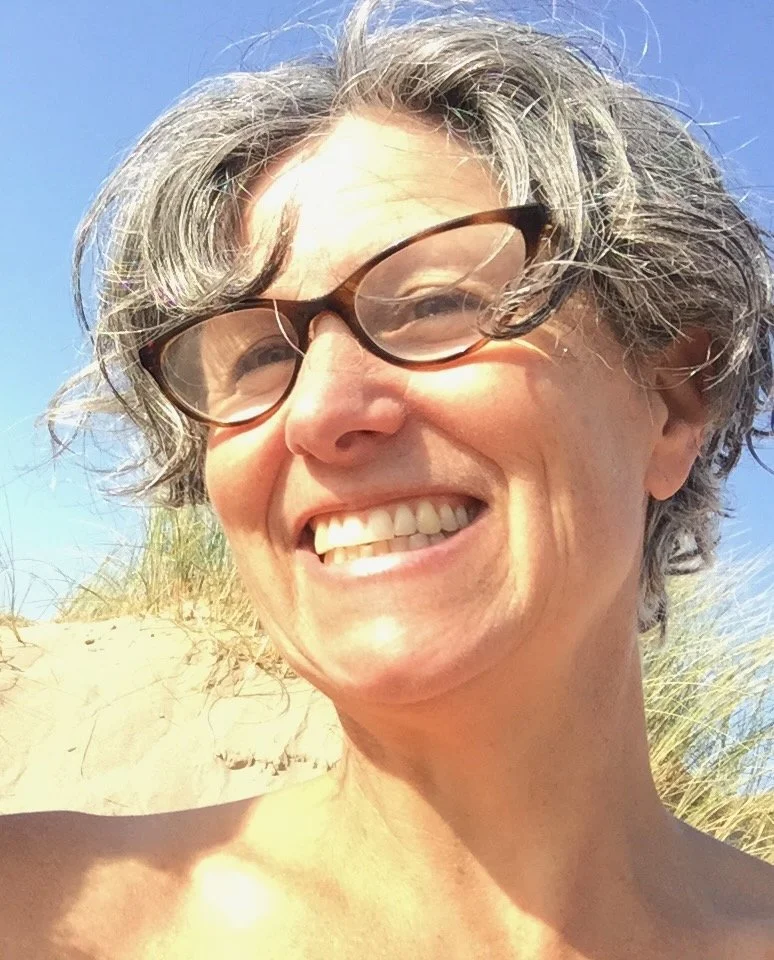 Giulia Holland wearing glasses, outdoors with sand dunes and blue sky in the background.