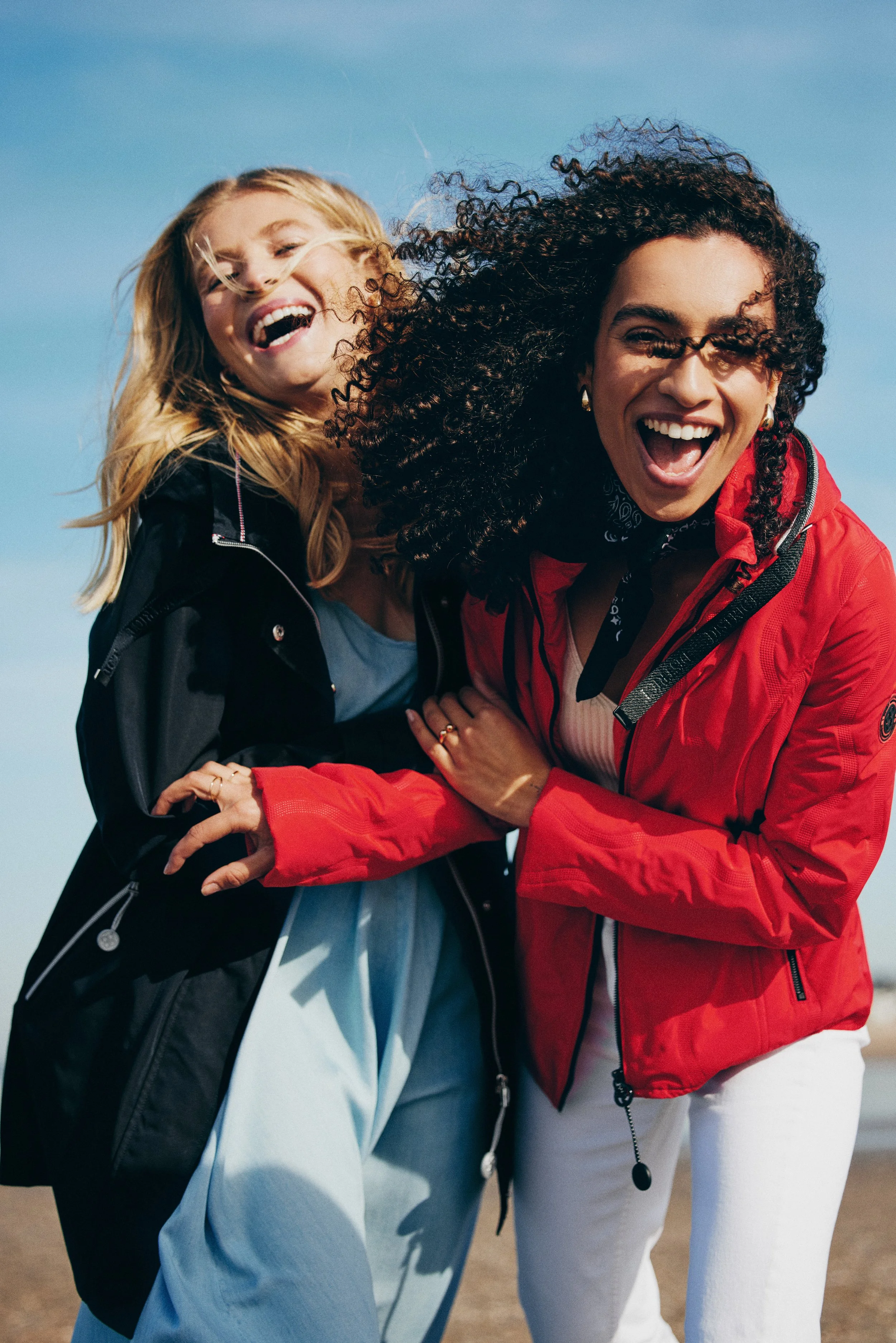Twee lachende vrouwen die samen plezier hebben buiten op een zonnige dag.