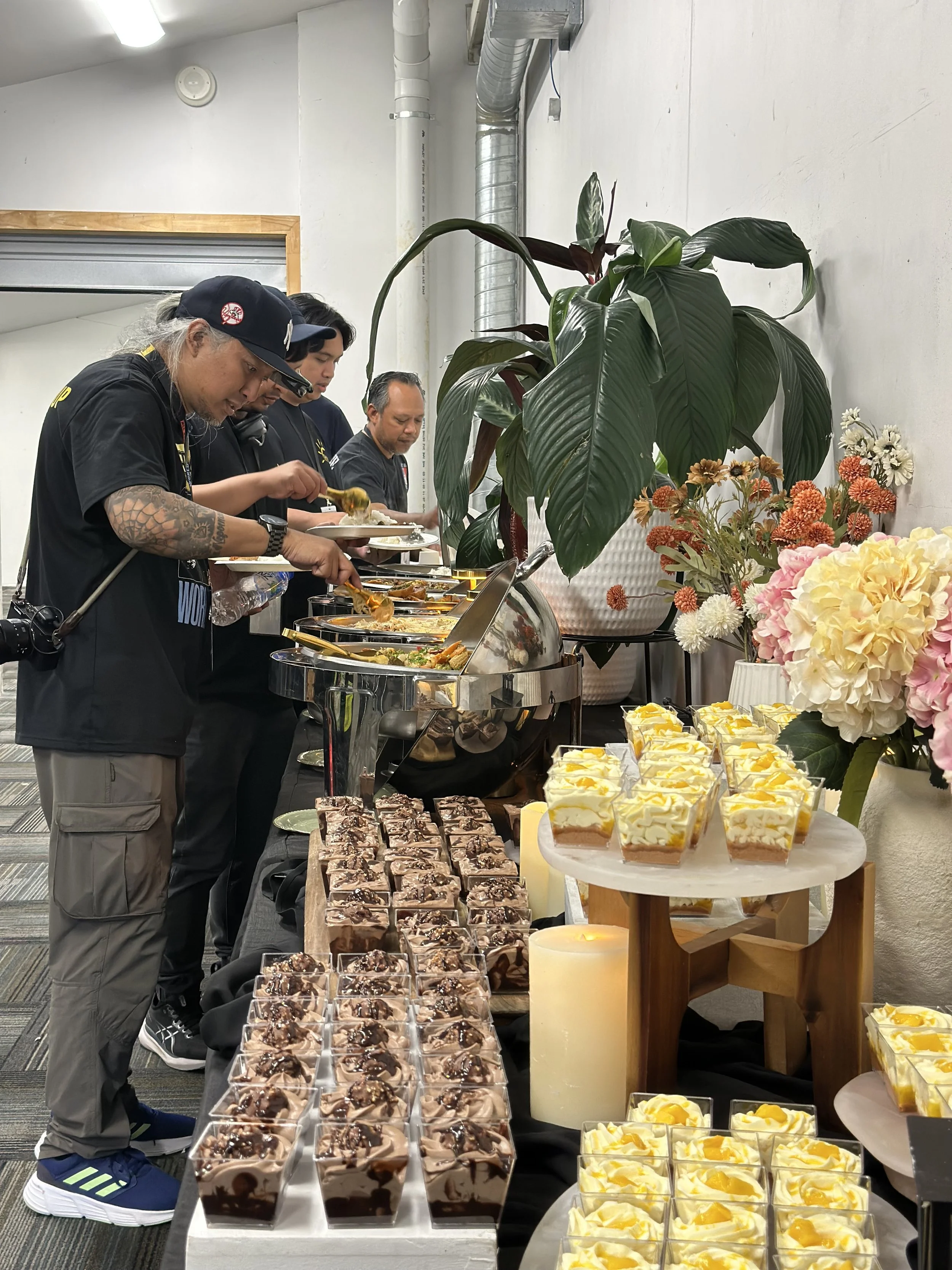 People serving themselves food at a buffet table with desserts and flowers. Catering for Eraserheads crew