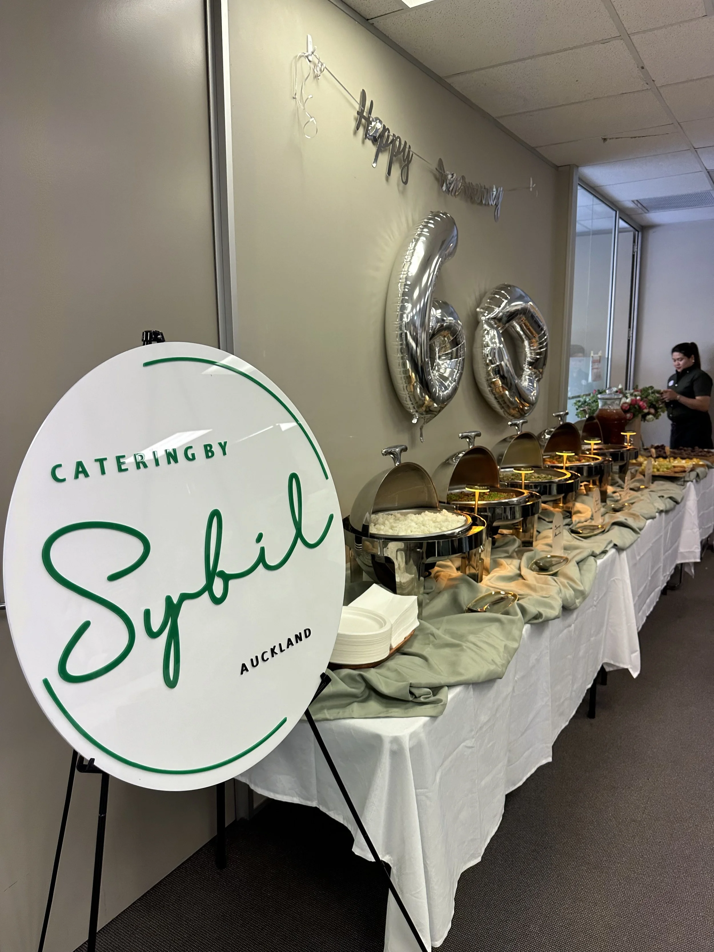 Buffet table at a celebration with large silver number balloons and a 'Happy New Year' banner in the background.