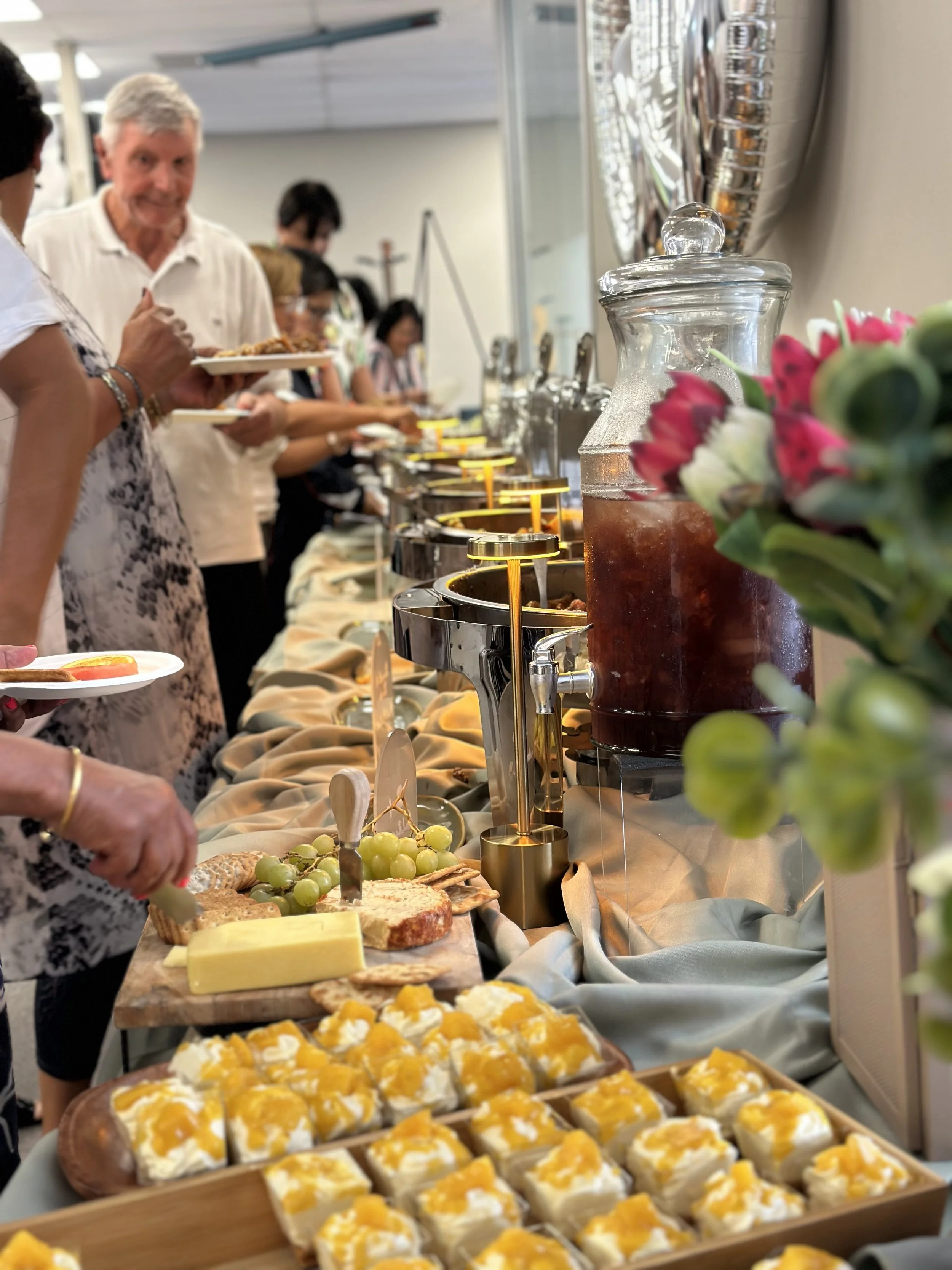 Buffet table with various foods and beverages at a social gathering, with people serving themselves.