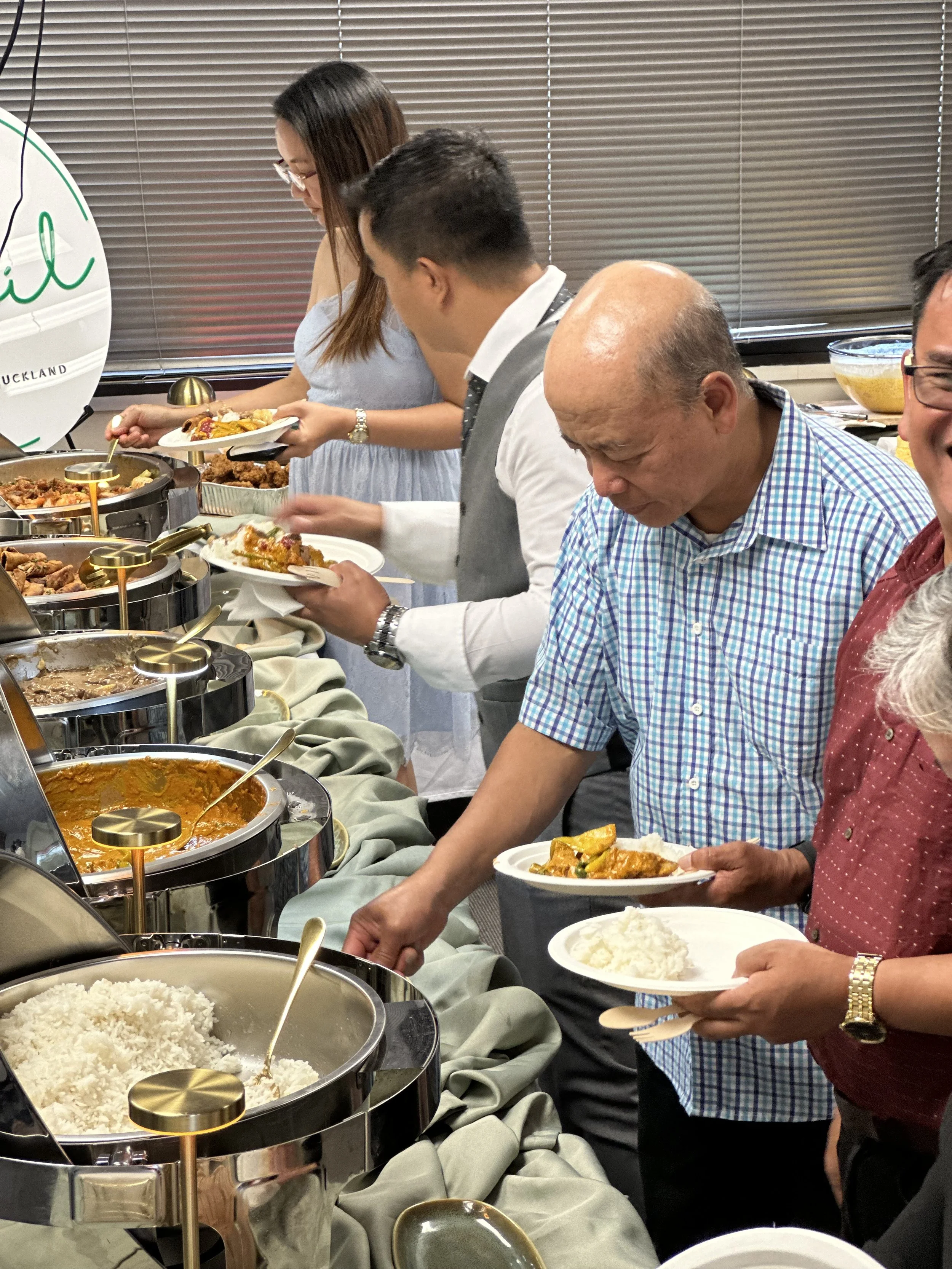 People serving themselves food from a buffet with rice, curry, and other dishes.