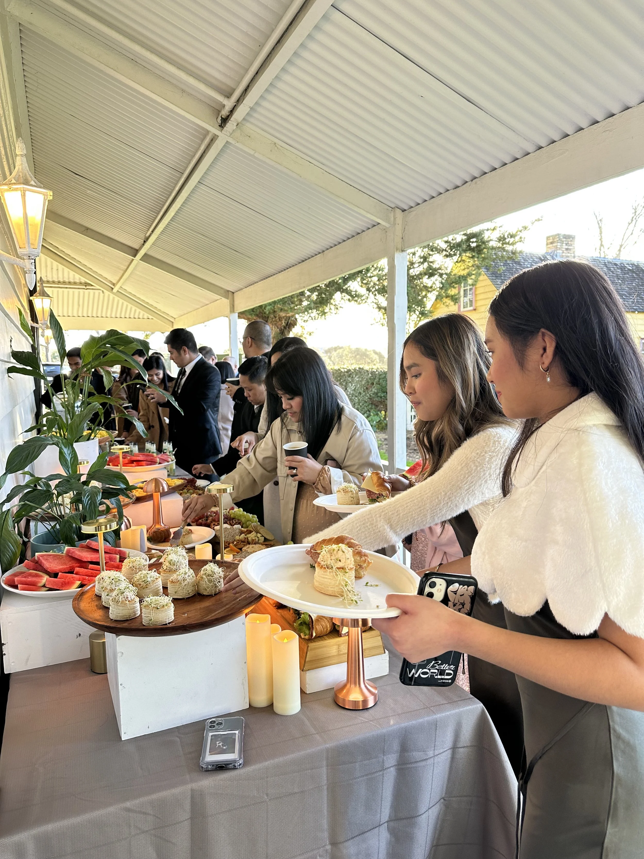 People at a buffet table serving themselves food at an outdoor event during the daytime.
