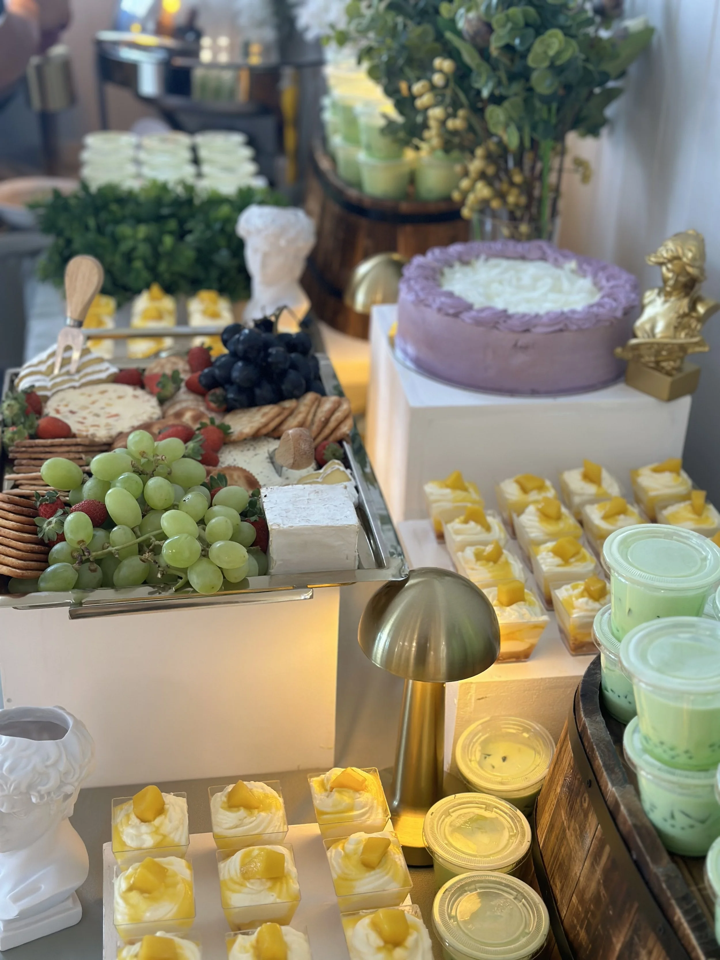A dessert table with a variety of treats including grapes, berries, crackers, cheese, cupcakes, and a purple cake decorated with white frosting and gold lion figurines.