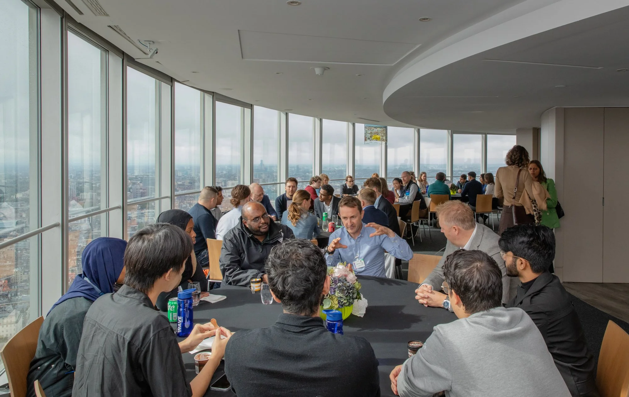 People sitting around a table in a high-rise building with a city view, engaging in a discussion.