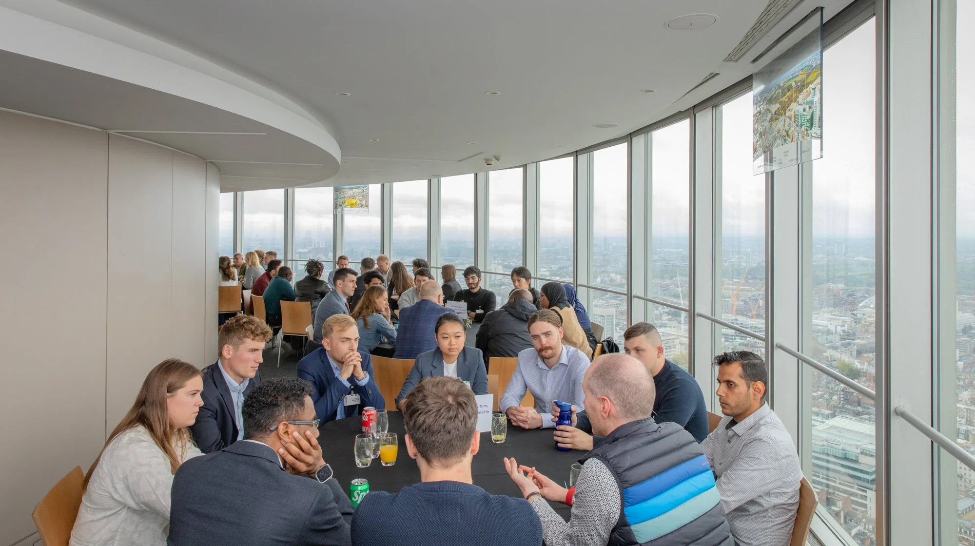 People sitting around a table during a business meeting or conference in a high-rise building with panoramic city views through large windows.