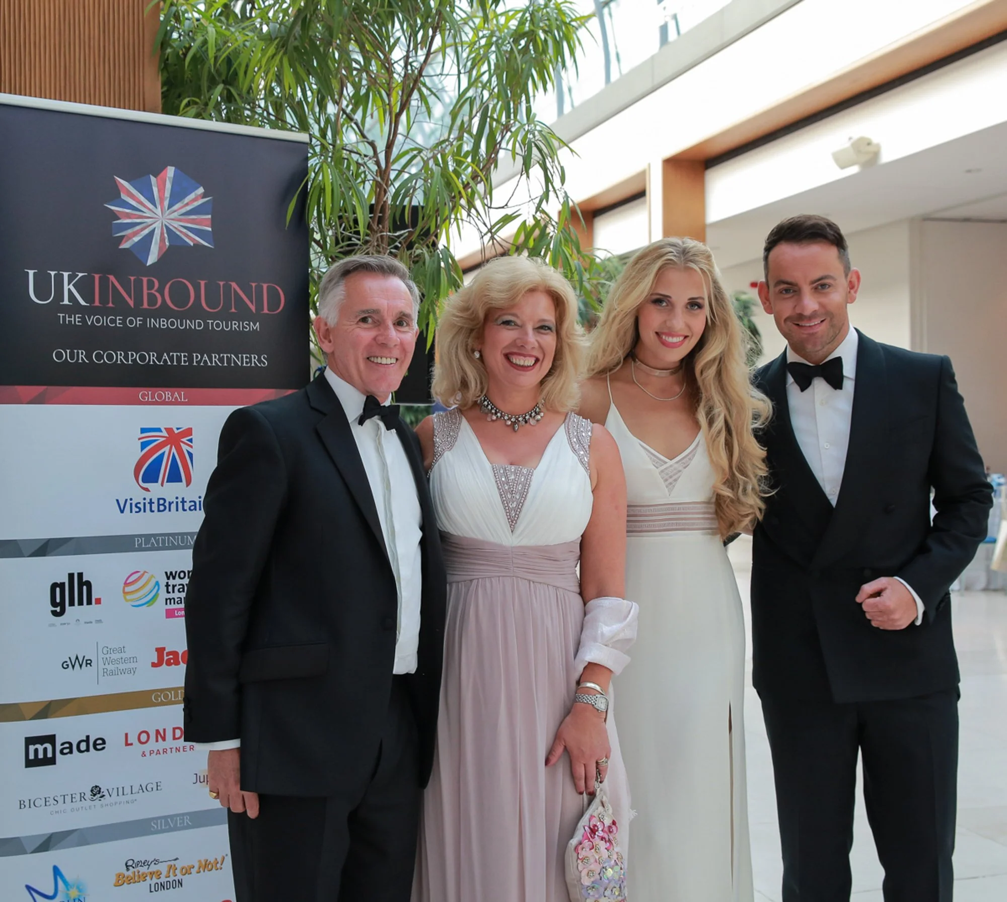 Four people at an event standing next to a UK inbound tourism banner, two men and two women in formal attire, smiling for the photo.