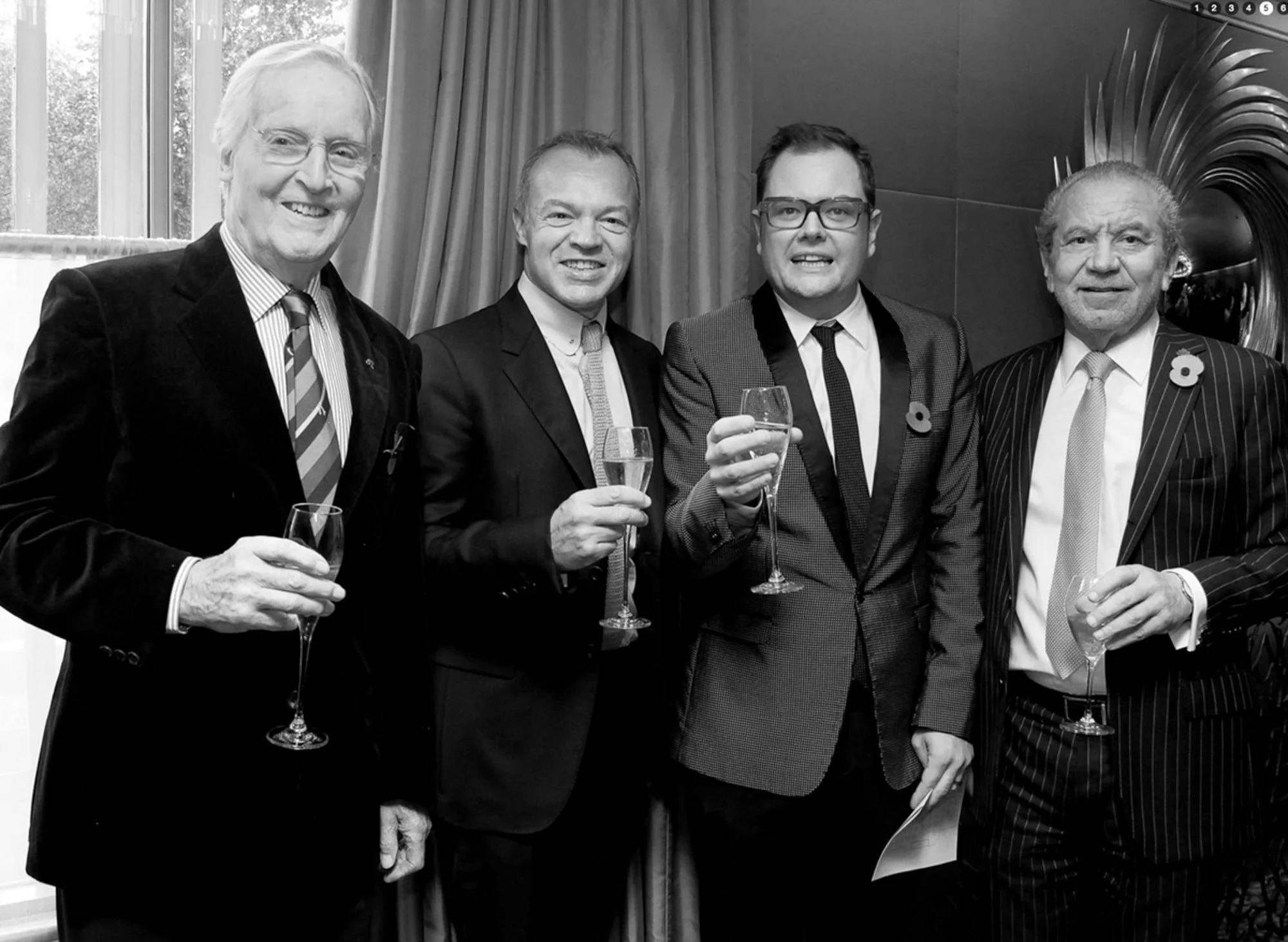 Five men in suits holding glasses of champagne during a formal event, standing in front of draped curtains and a decorative mirror.