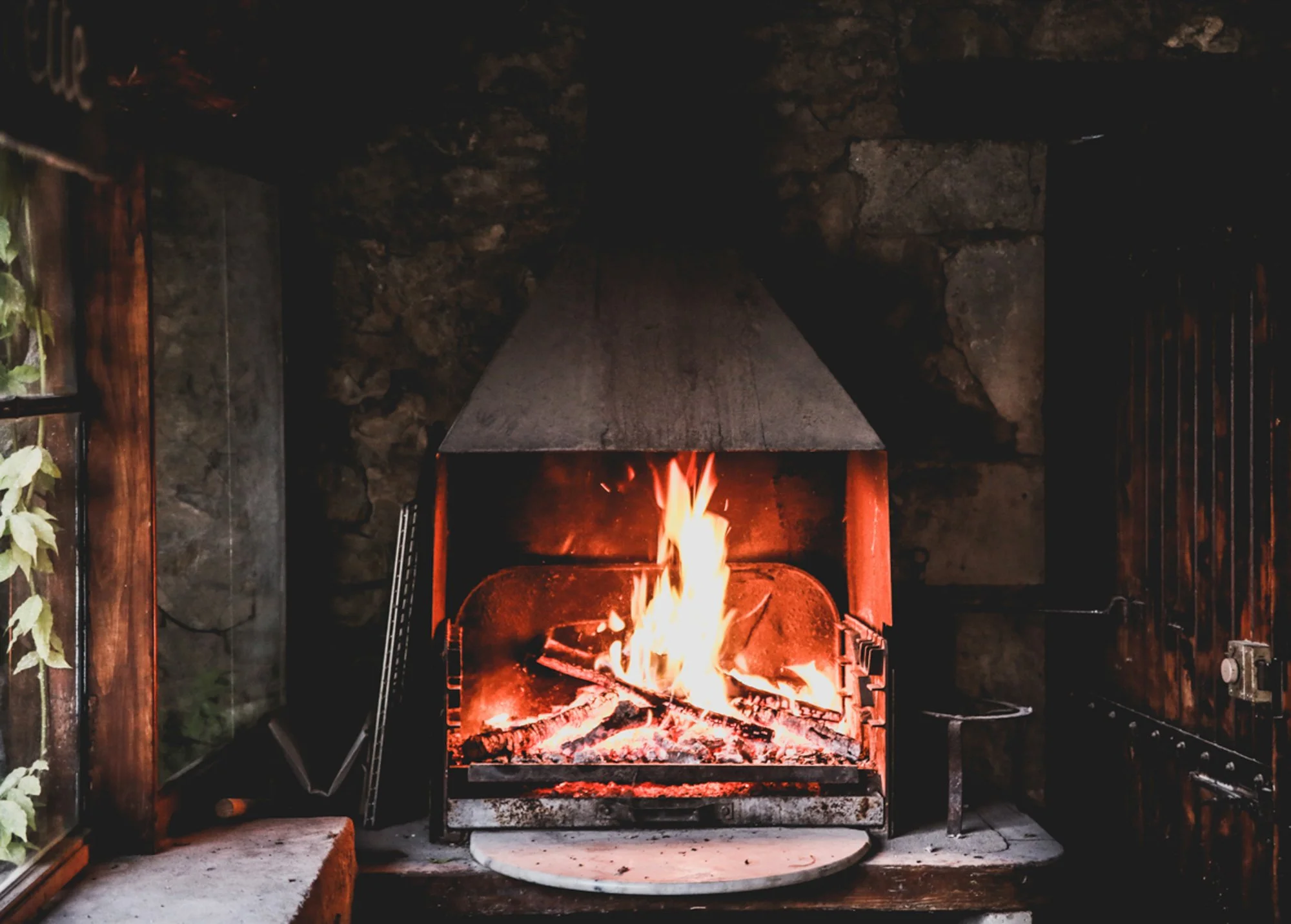 A cozy fireplace with a roaring fire, set in a rustic stone and wood interior.