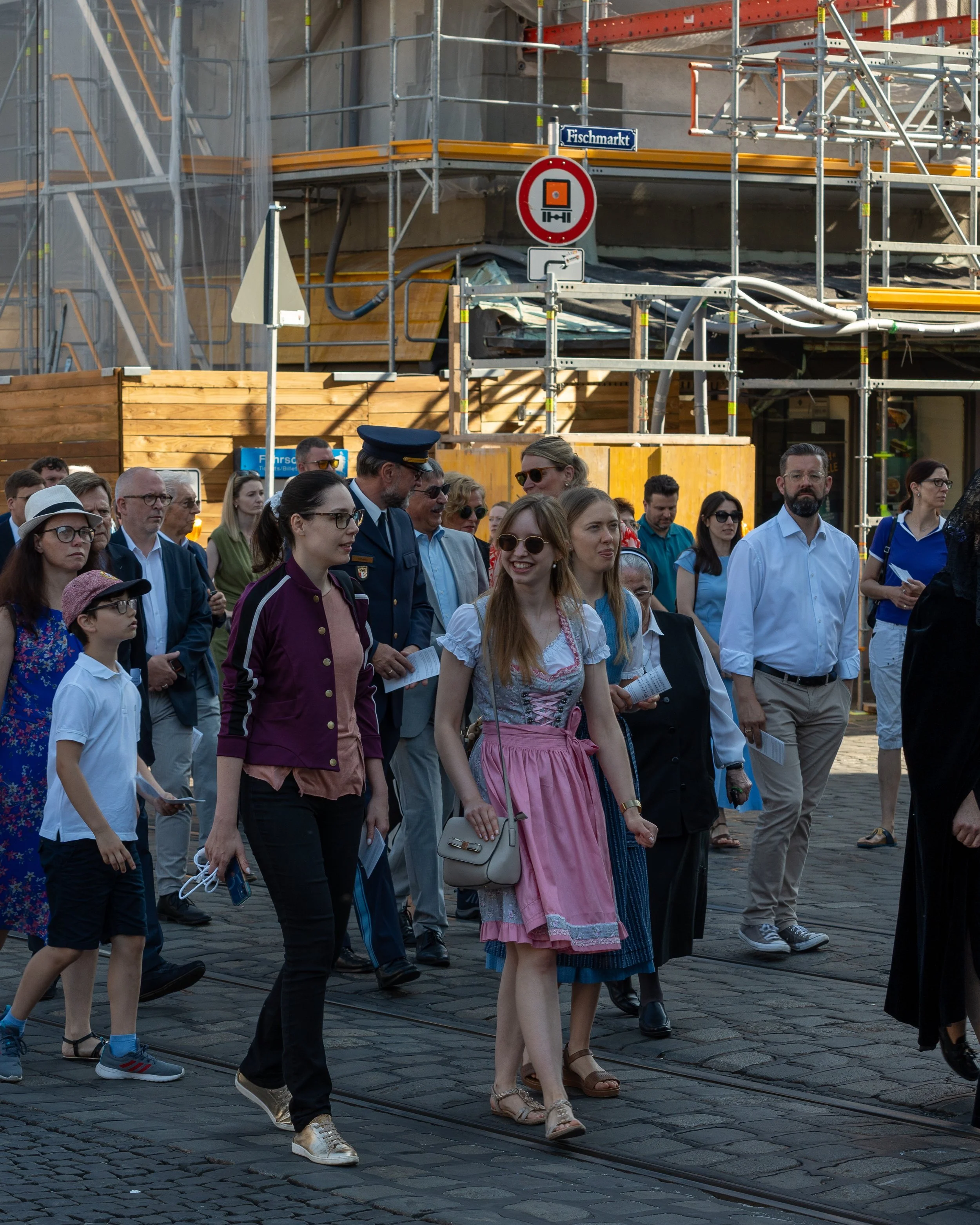 Group of people walking on cobblestone street near construction site with scaffolding and wooden barriers in the background.