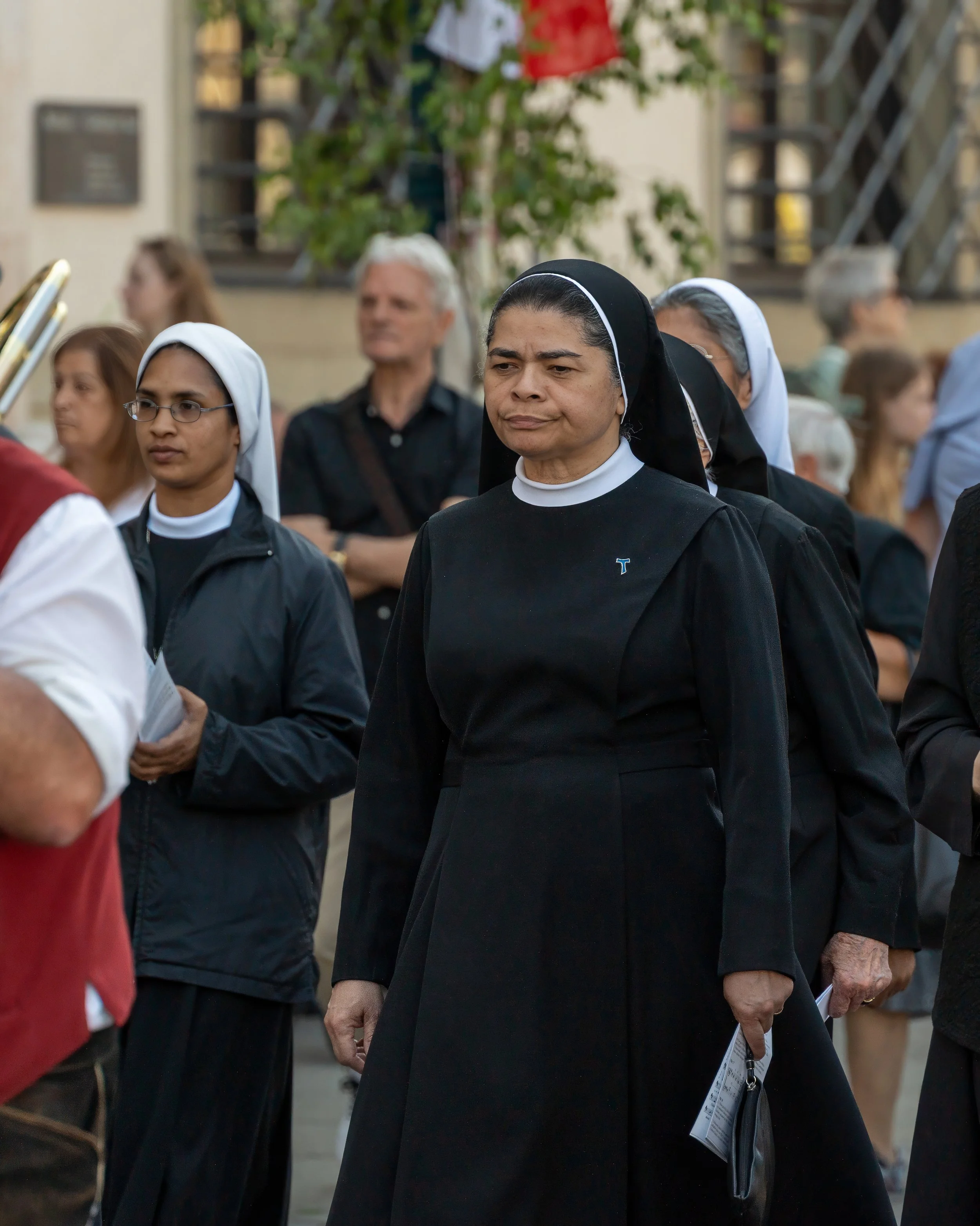 A group of nuns and religious women marching in a procession, with solemn expressions, outside during daytime.