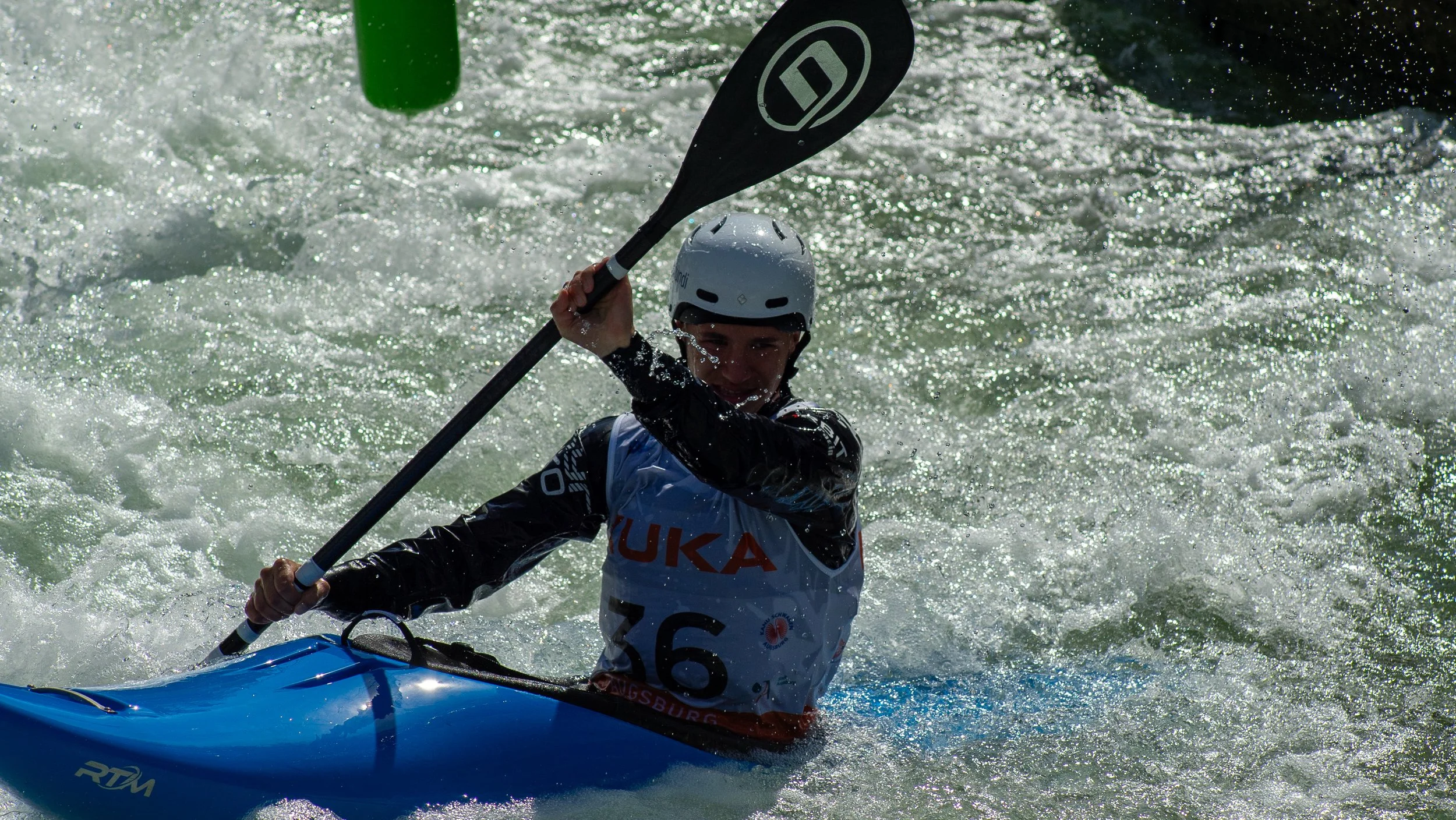 A kayaker wearing a helmet and life vest paddling through whitewater rapids.