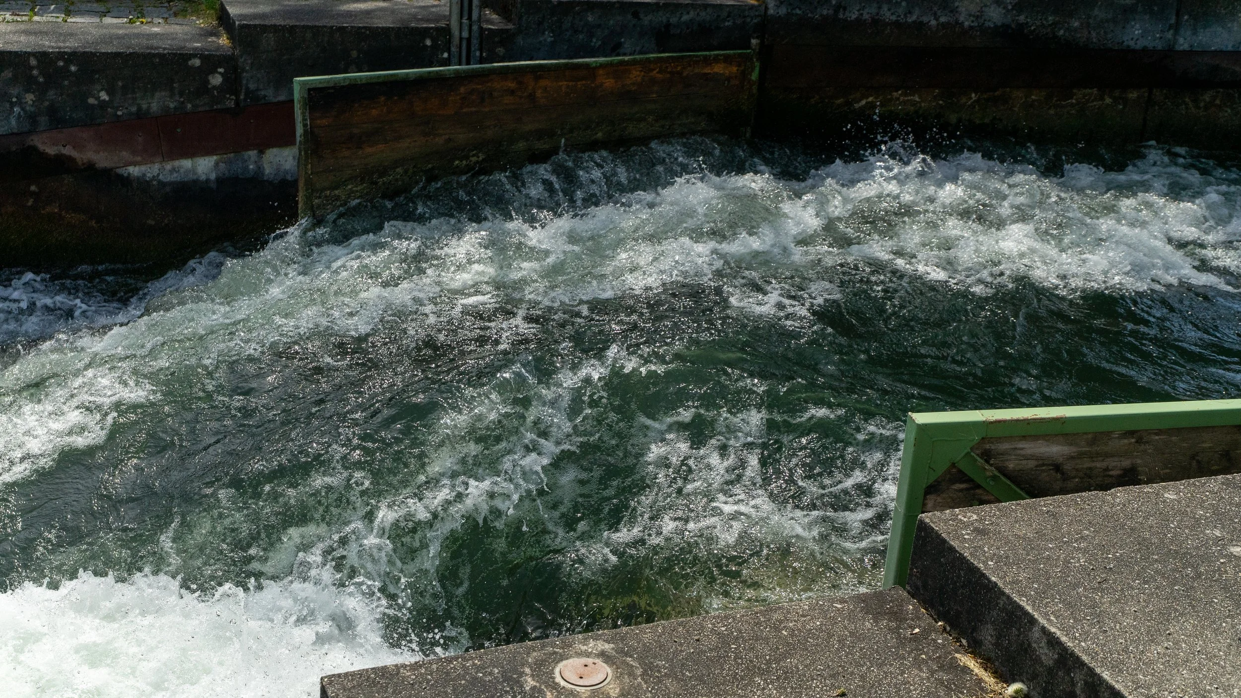 Fast-moving water flow in a canal or waterway with wooden barriers on the sides.