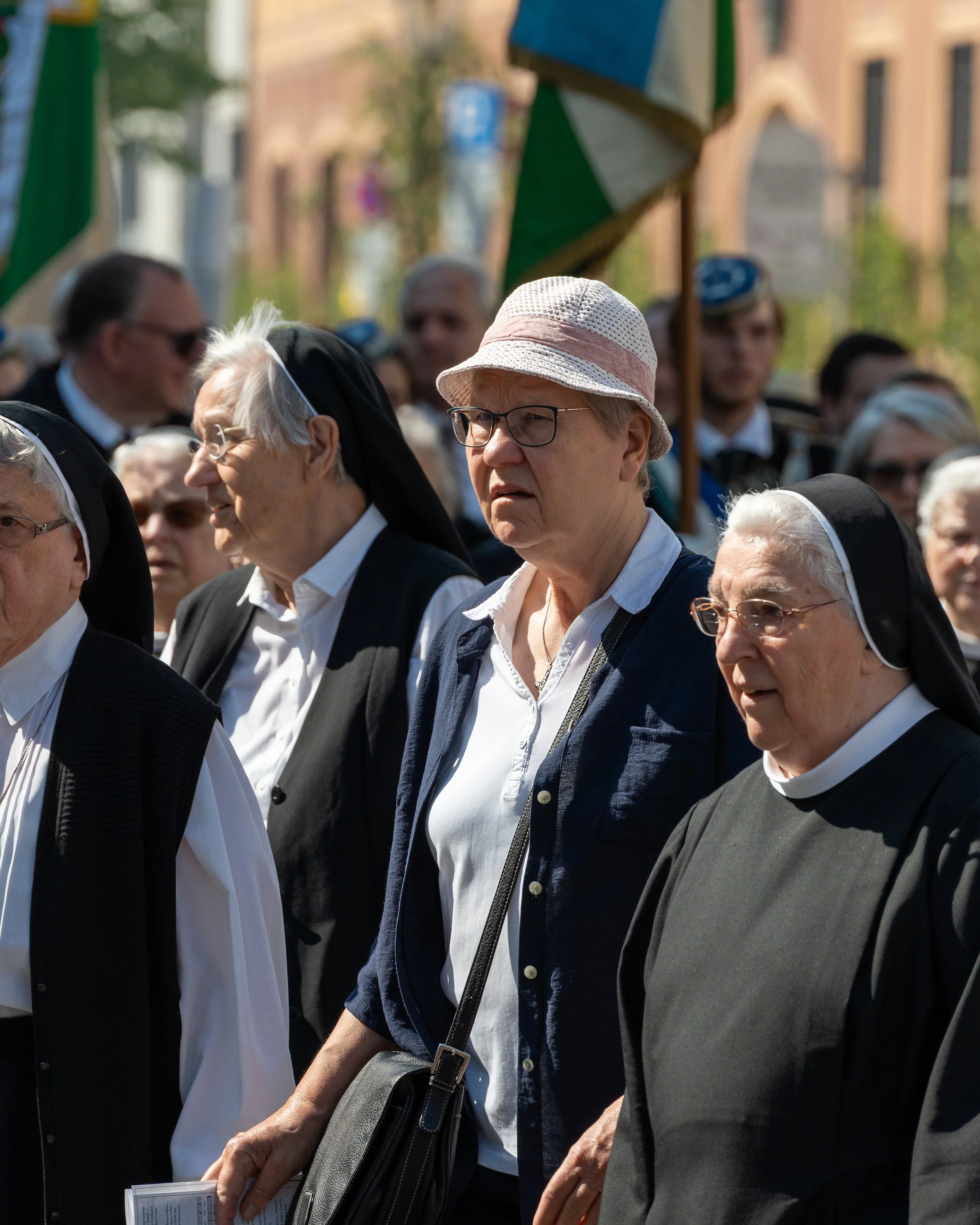 A group of elderly women, including nuns, participating in a public event or march outdoors during daytime. They are dressed in religious and casual clothing, with some wearing glasses and hats.