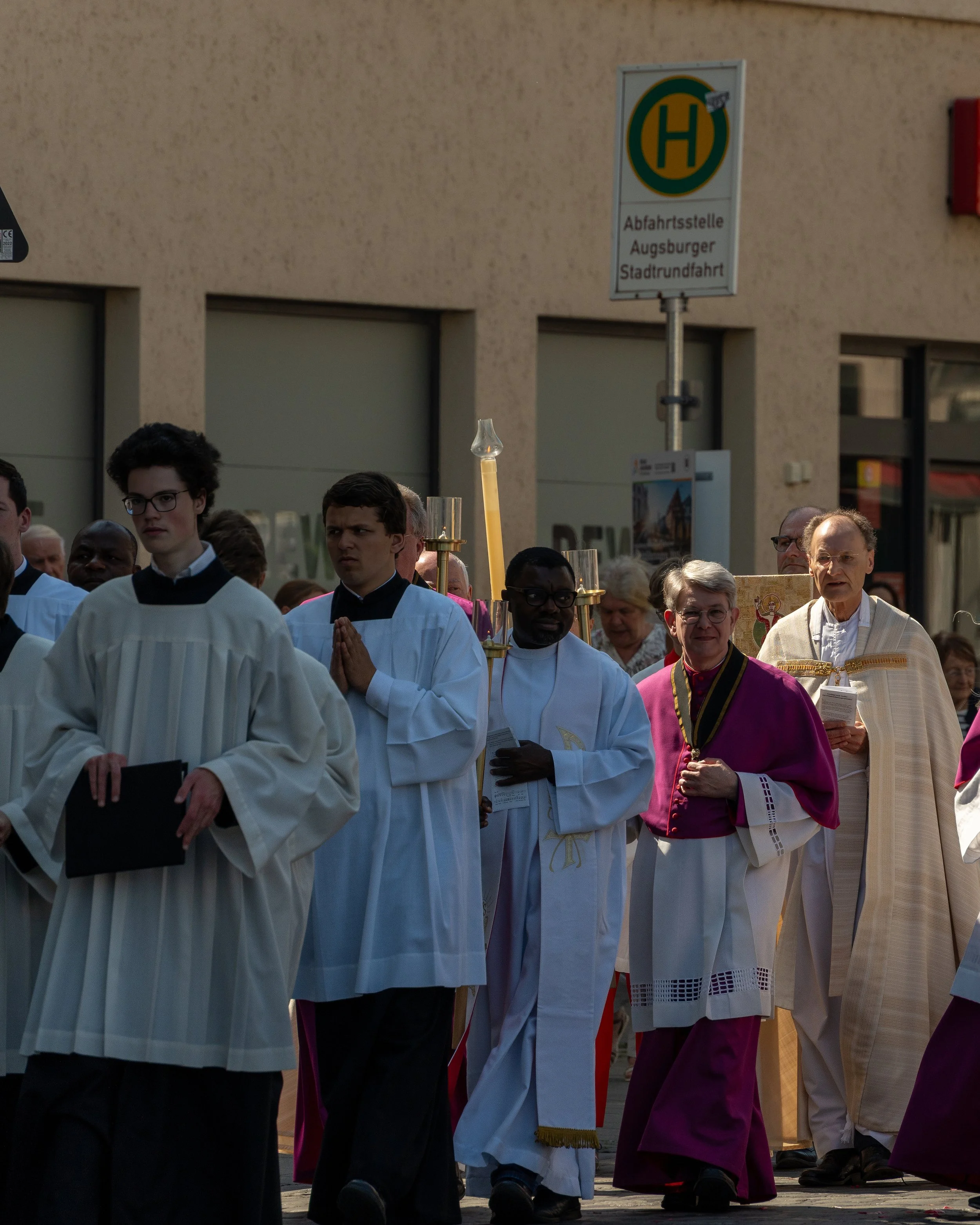 clergy and altar servers participating in a religious procession on a city street