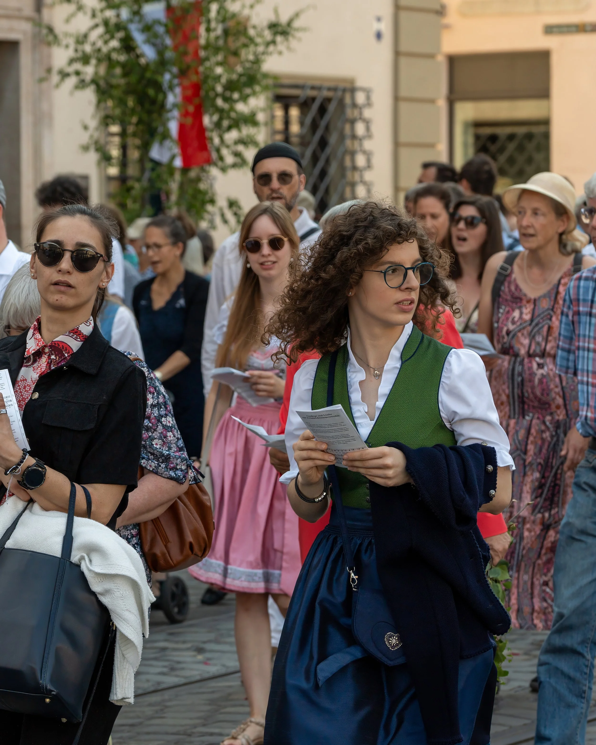Crowd of people walking outdoors on a city street, some holding papers, dressed in casual and traditional attire.