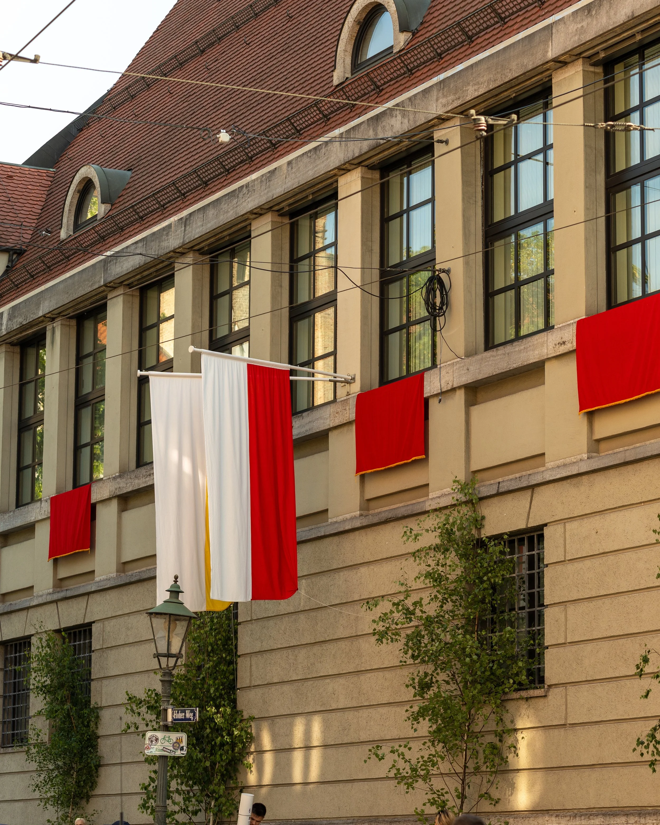 Building with large windows, red and white curtains hanging from a line, and small trees in front. A street sign and street lamp are visible below.