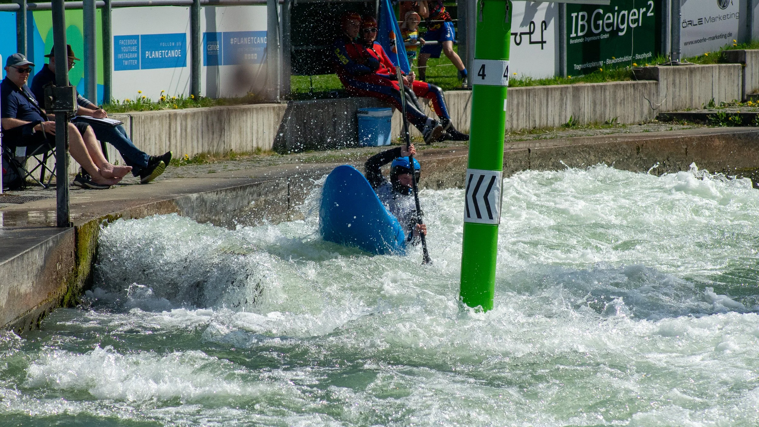 People watching a kayaker overturn in a whitewater course during a kayaking event.