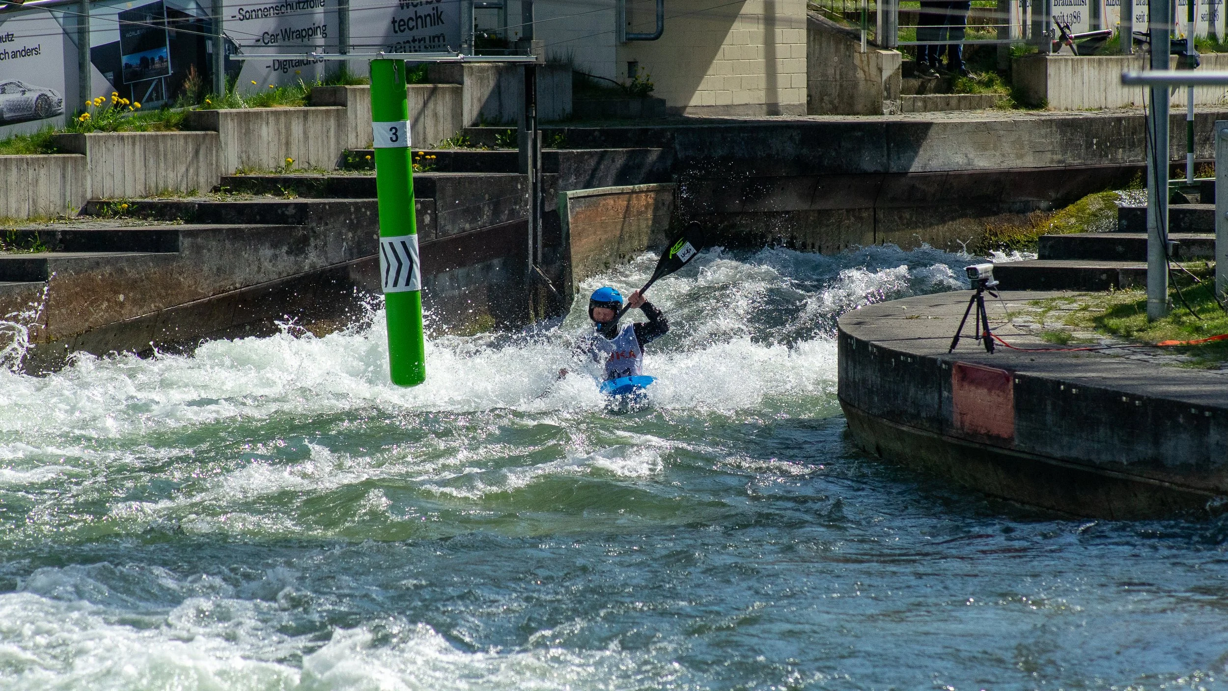 A person kayaking in turbulent water near a concrete structure with stairs and railings.