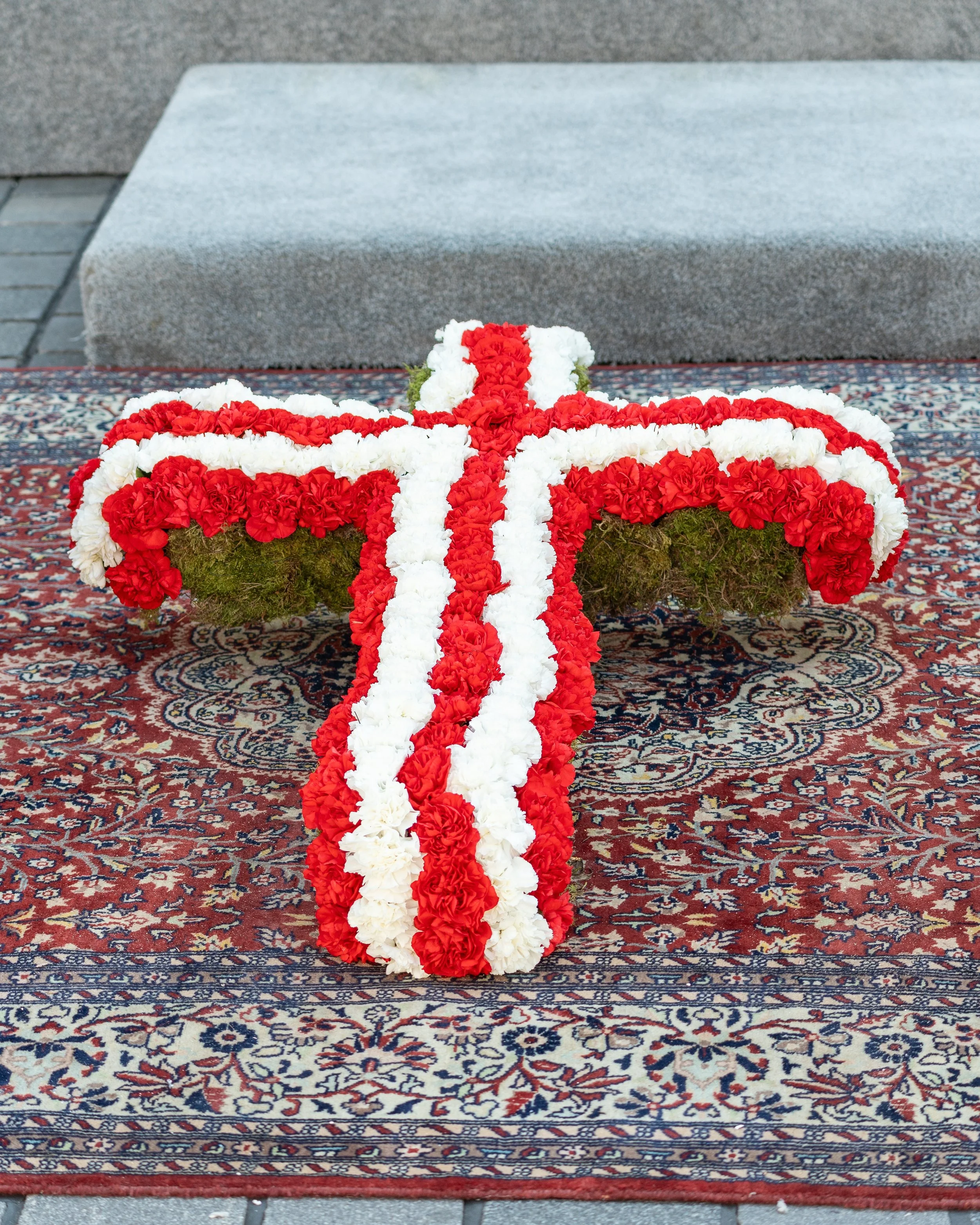 A floral cross made of red and white flowers on an ornate rug.