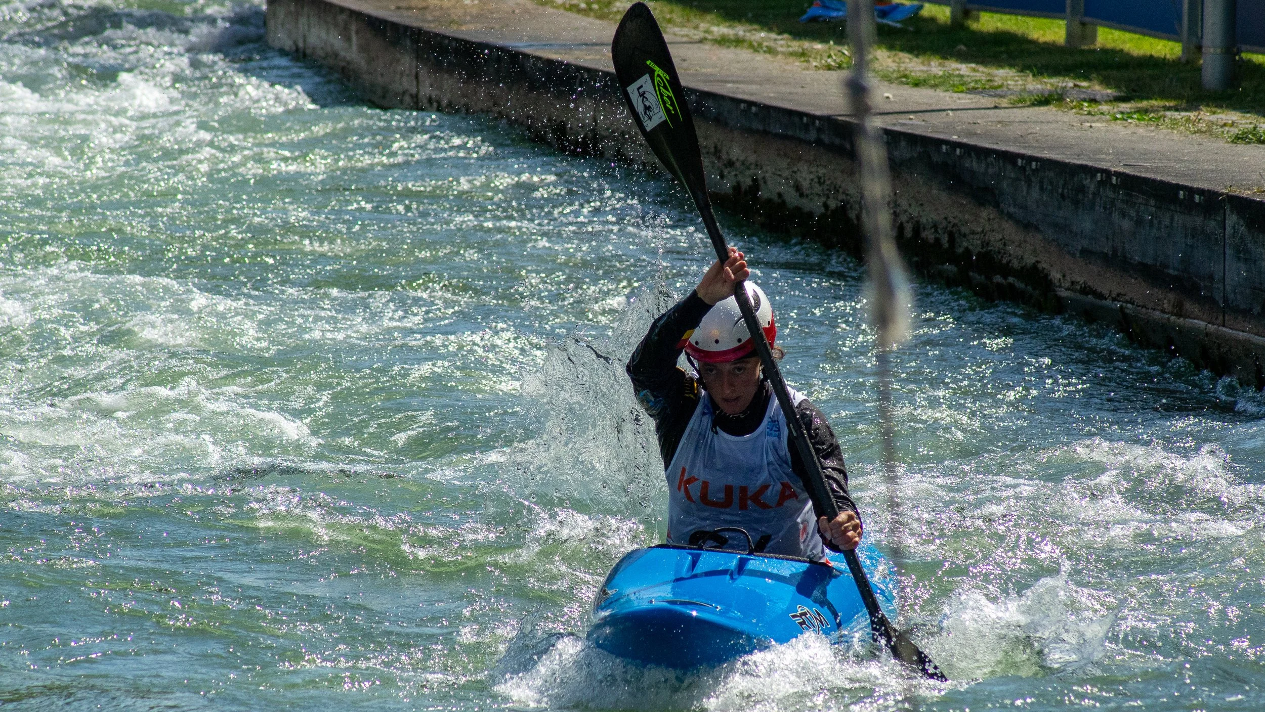 Person wearing a helmet and a life vest kayaking in white water river.
