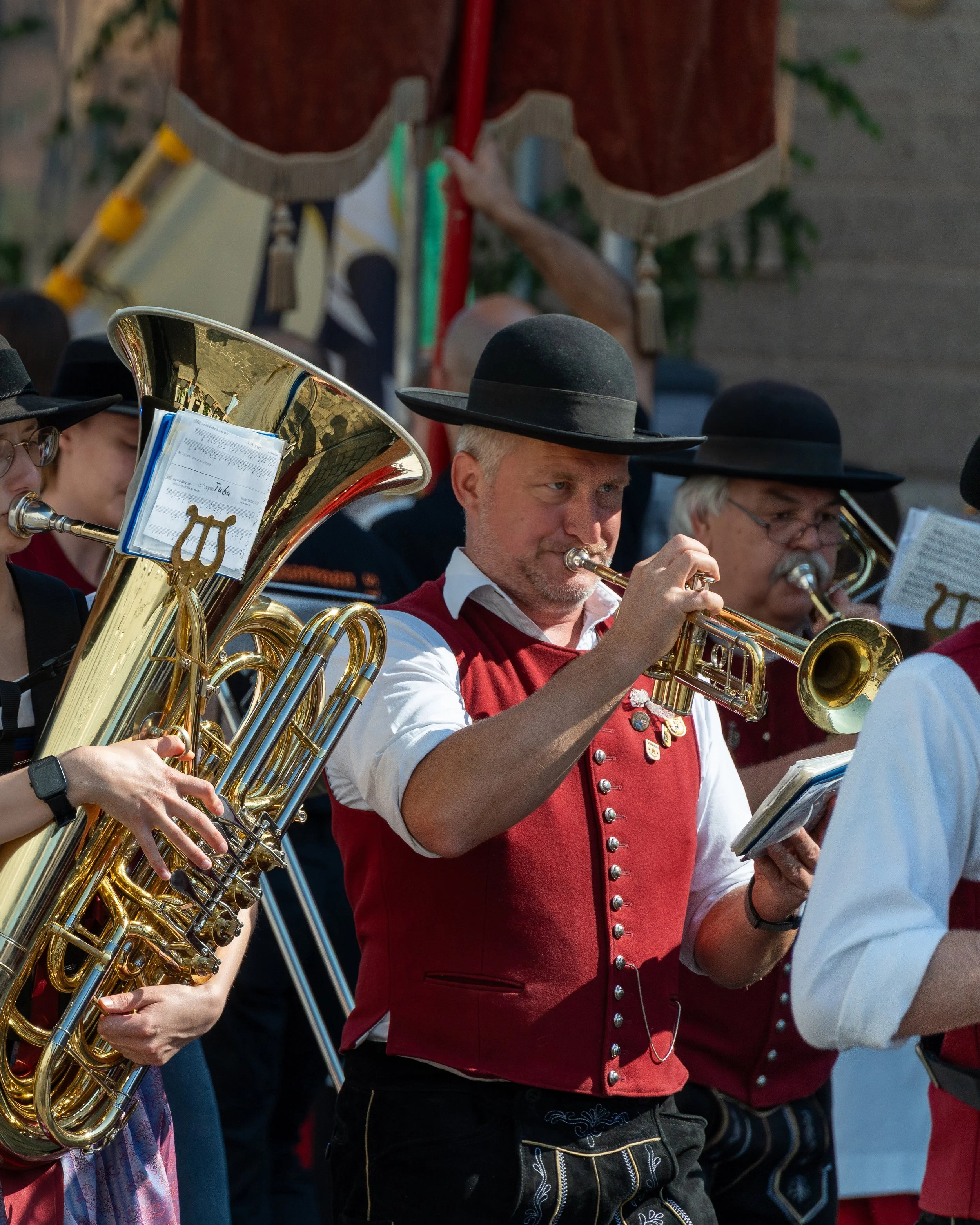 A group of musicians dressed in traditional Bavarian attire, playing brass instruments at an outdoor event.