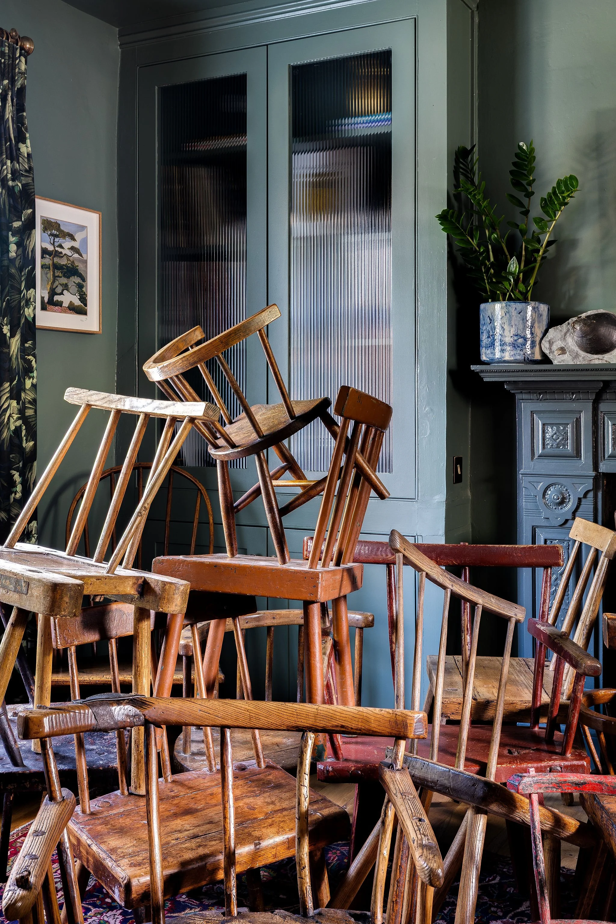 A room filled with stacked wooden chairs in front of a green wall and cabinet.