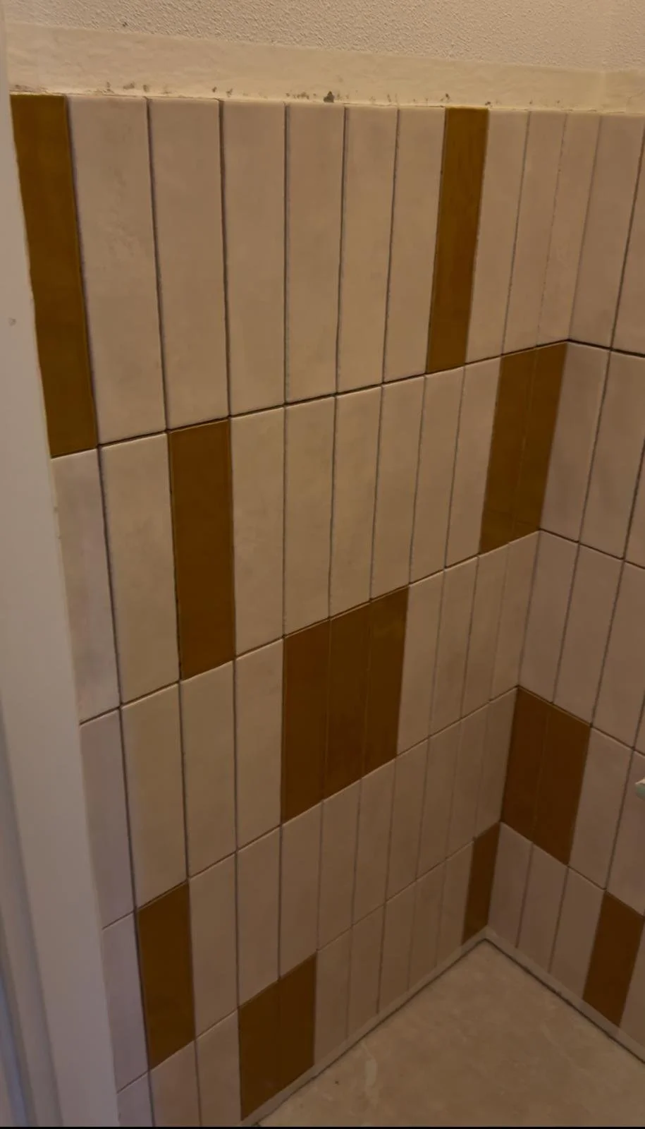 Corner of a tiled wall with beige and brown rectangular tiles arranged in a pattern.