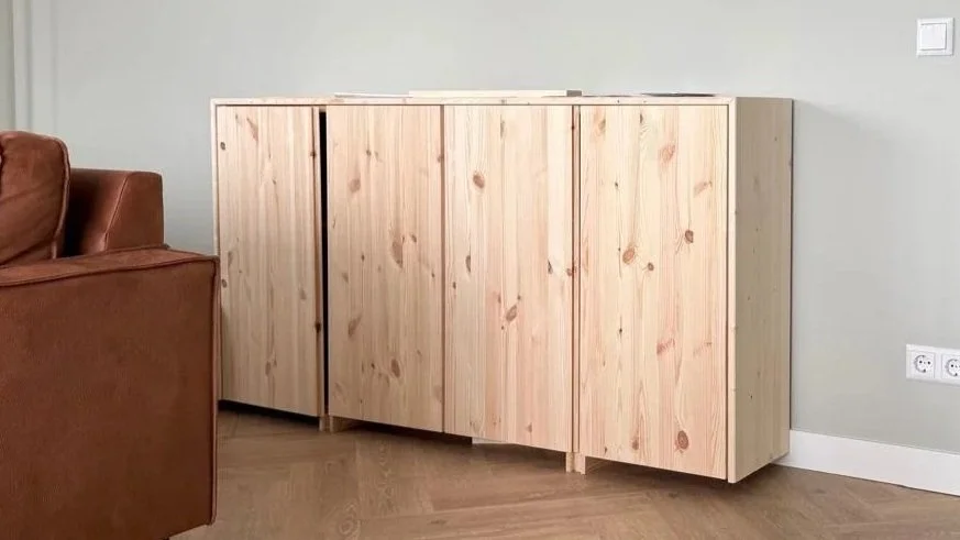 Onbehandelde houten kast met vier deuren, naast een bruine leren bank in een kamer