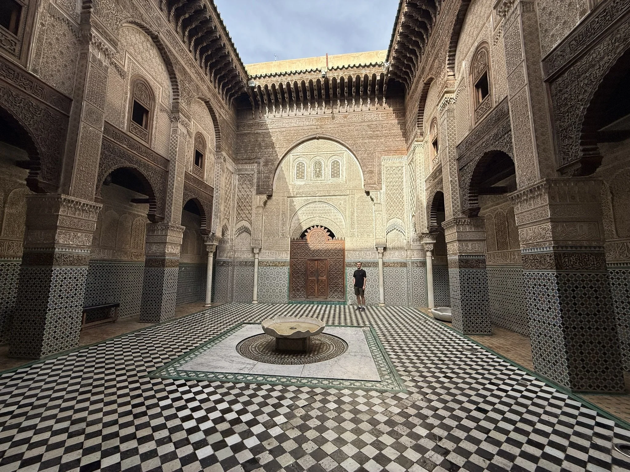 Interior courtyard with ornate Moroccan architecture, intricate tile work, and a central stone fountain.