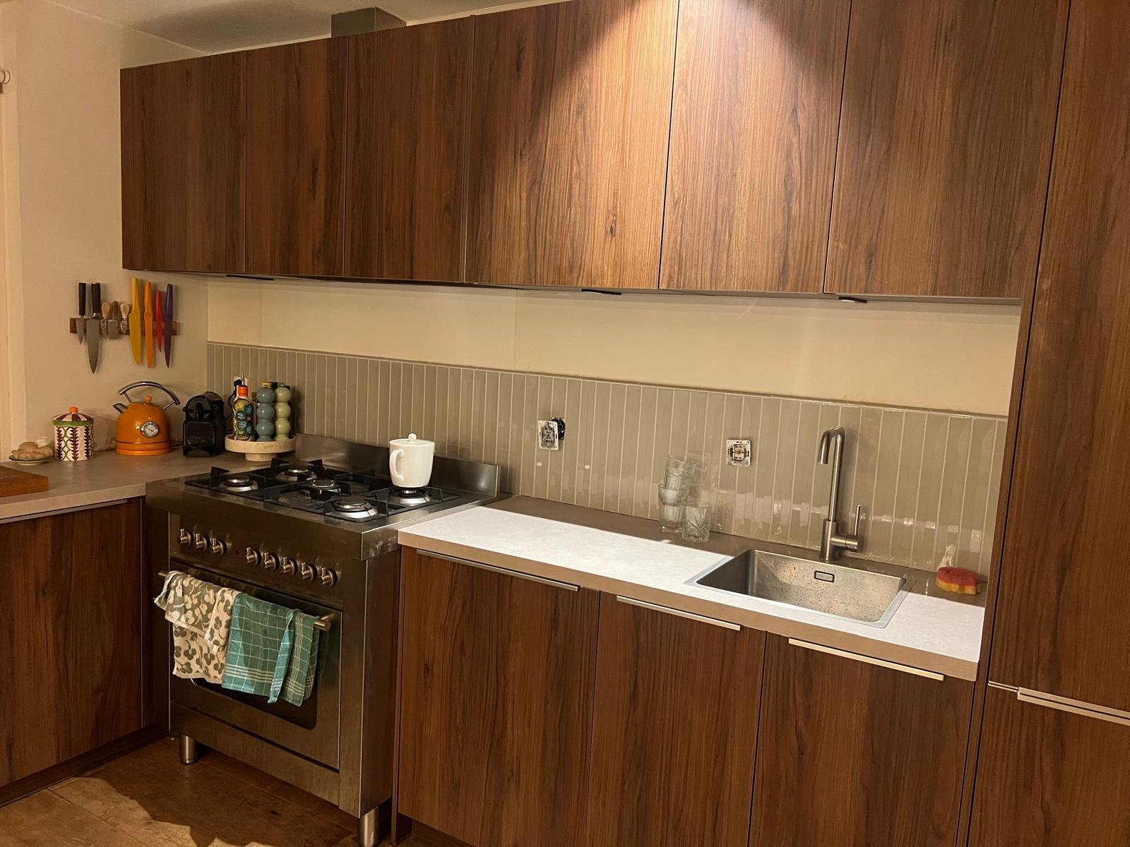 Een keuken met houten keukenkasten, een fornuis, een gootsteen, en diverse keukenspullen op het aanrecht.