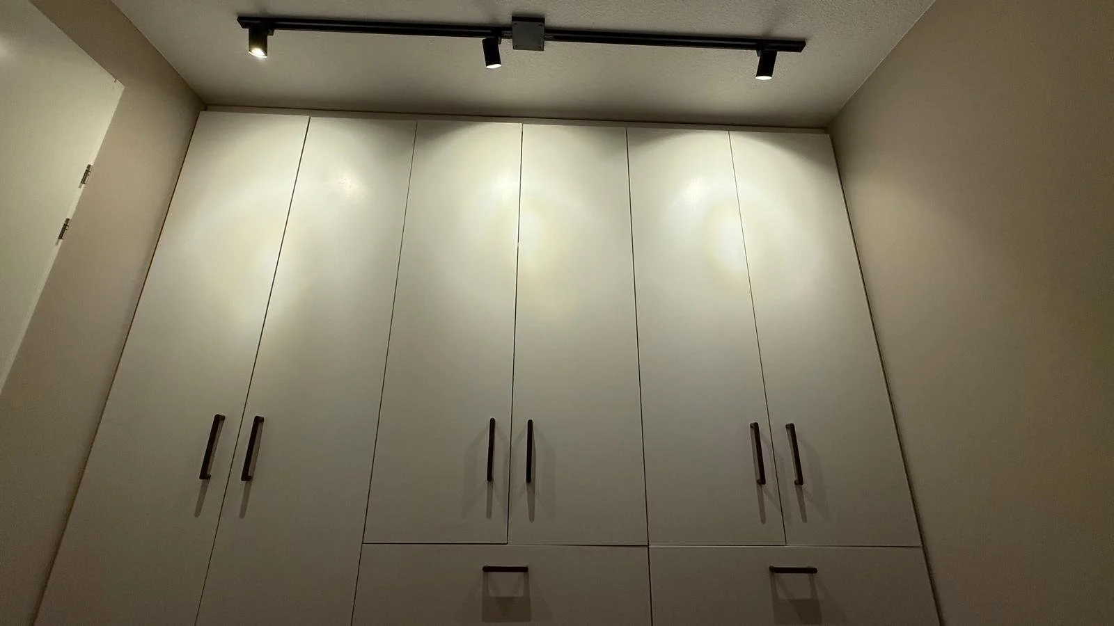 Grote witte kast met zwarte handgrepen onder een plafond met plafondlampen.