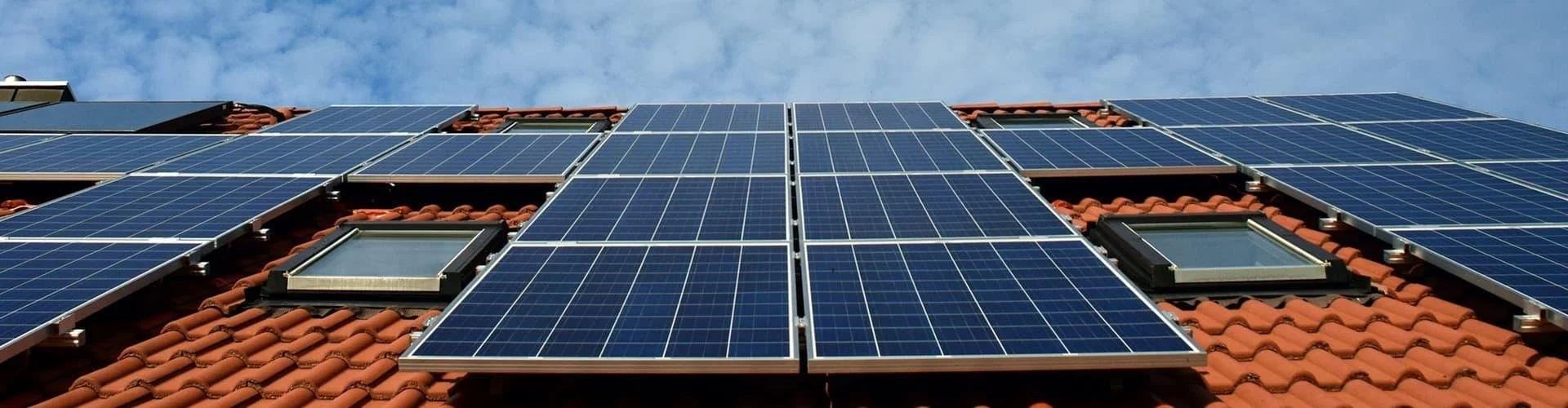 Dach mit mehreren Solarmodulen und Dachfenstern unter blauem Himmel.