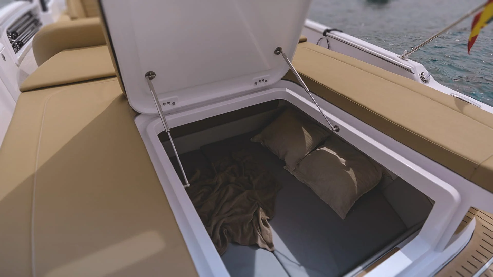 Open storage compartment on a yacht with pillows and bedding inside, with water visible in the background.