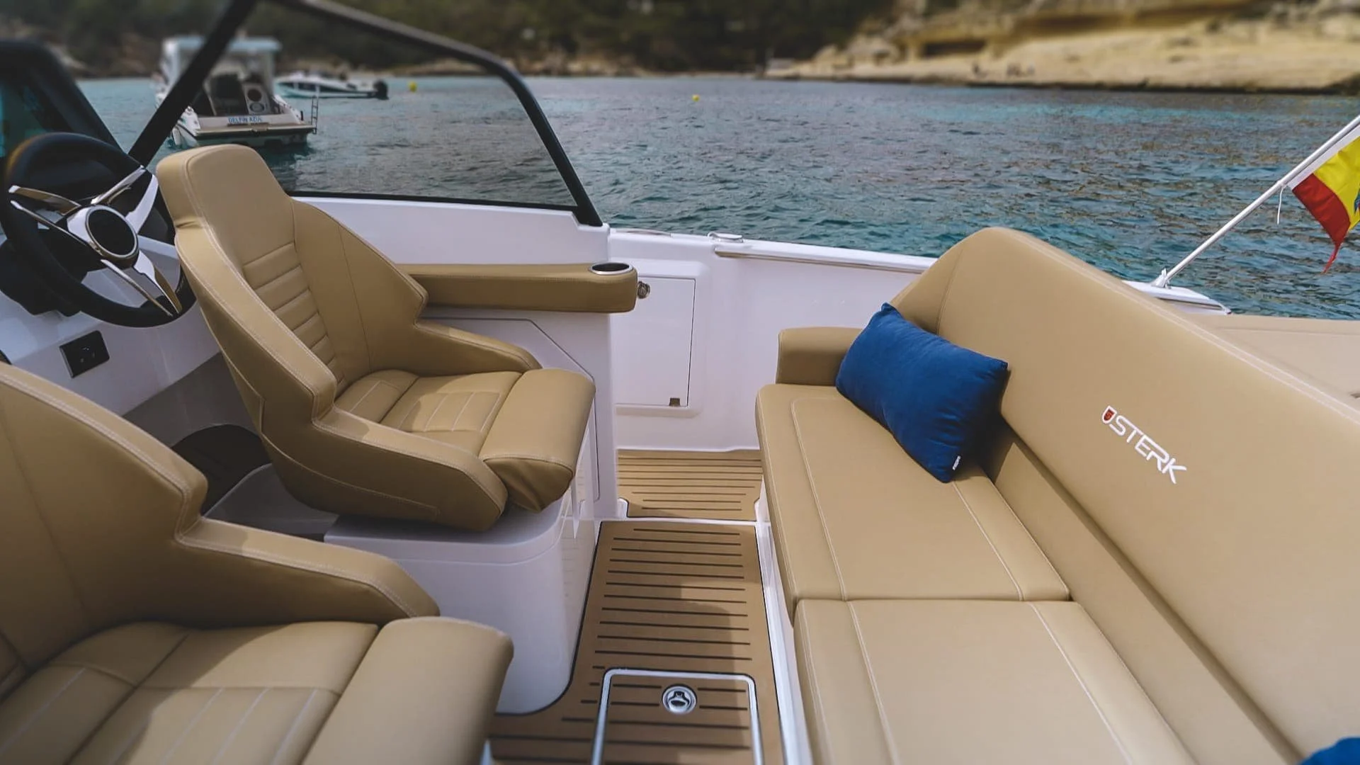 Interior view of a boat with beige leather seats, a blue cushion, and a view of the water and other boats in the background.