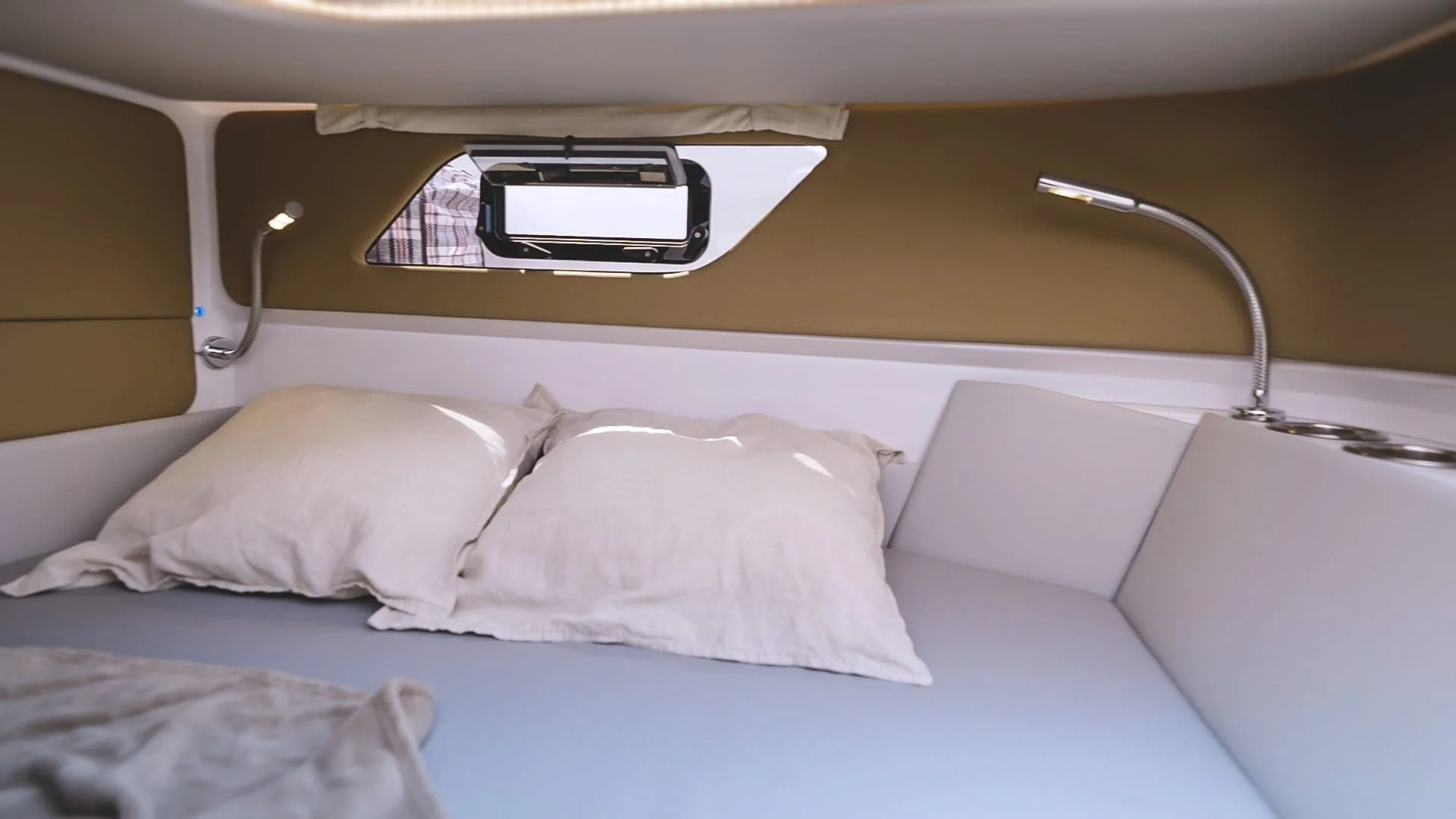 Interior of a small boat cabin with a bed, beige pillow, small window, and two flexible reading lights. Sterk 31RC Supersport