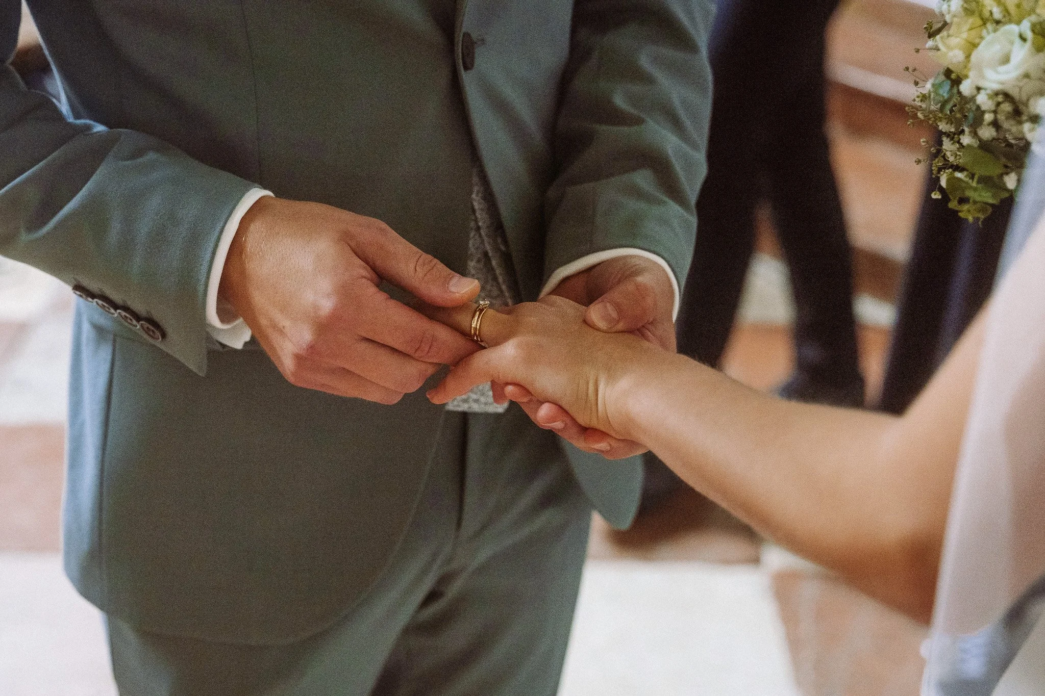 Hände bei einer Hochzeitszeremonie, während der Bräutigam den Ring an den Finger seiner Braut ansteckt.