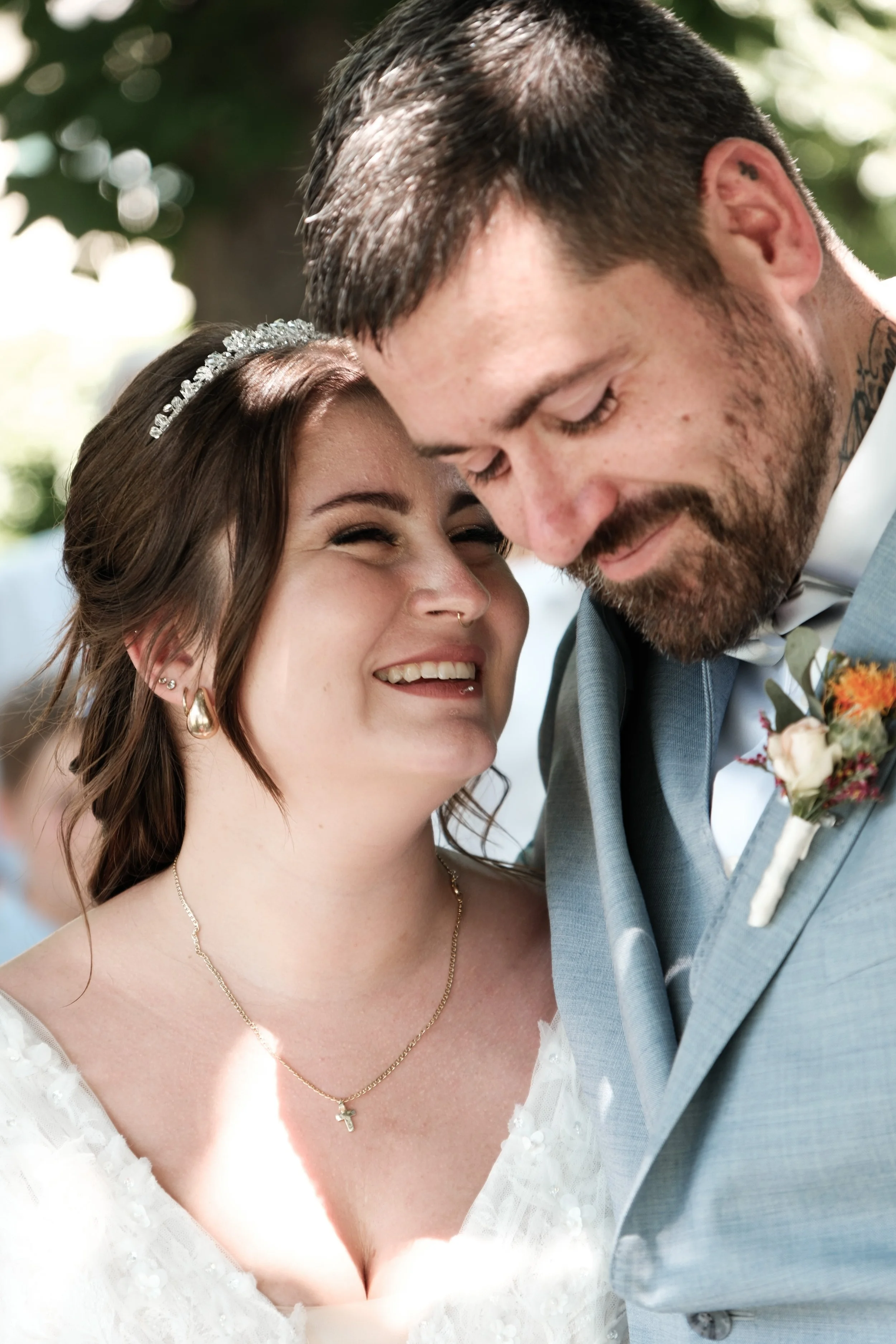 Ein frisch verheiratetes Paar bei einer Hochzeit, die eng umschlungen sind und liebevoll in die Augen schauen, im Freien mit Sonnenlicht und Bäumen im Hintergrund.