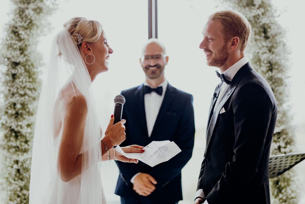Braut und Bräutigam bei ihrer Hochzeitszeremonie, mit einem freien Trauredner im Hintergrund.