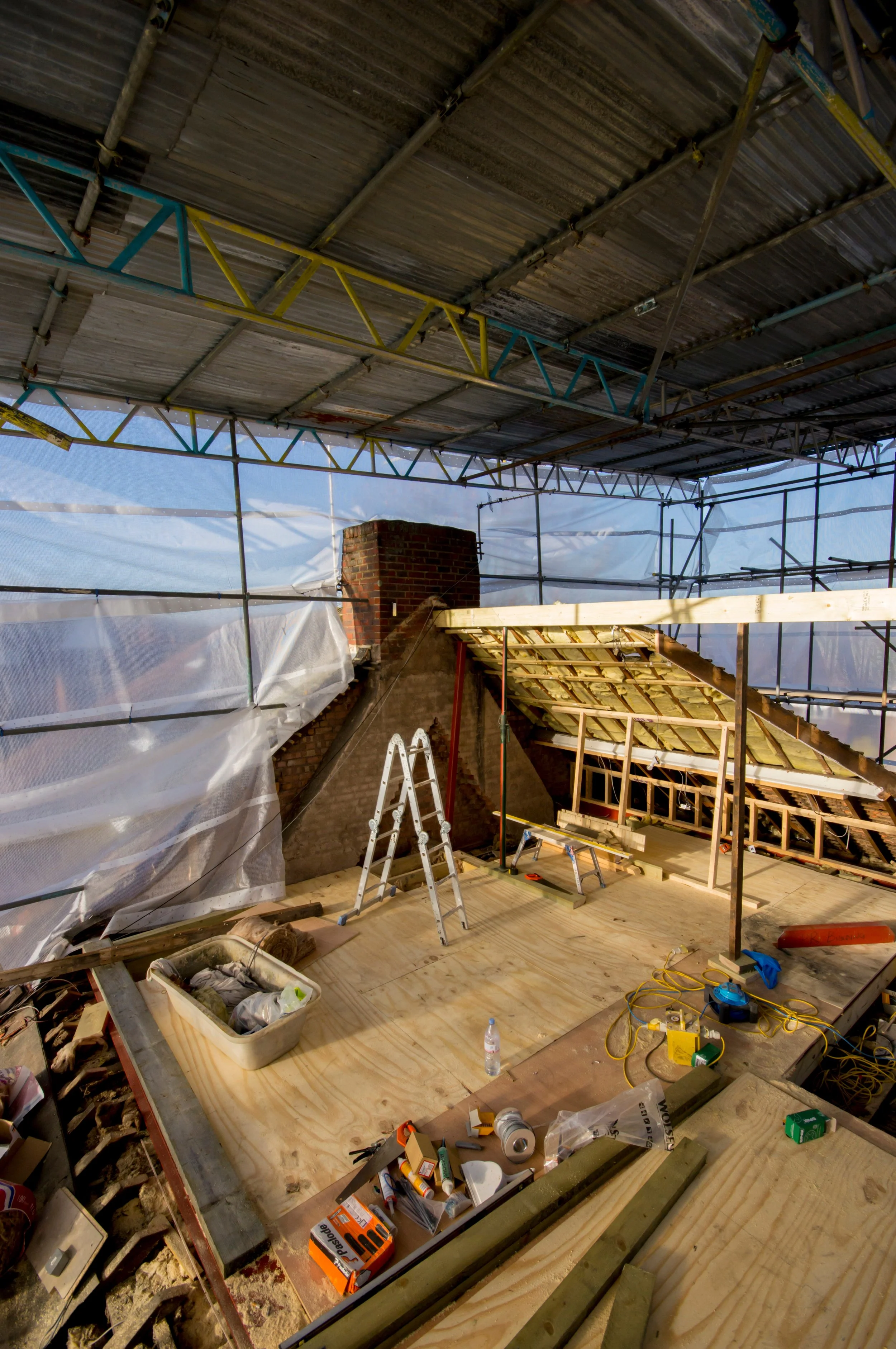 View of an attic under renovation with construction tools, a ladder, and partially finished roof structure.