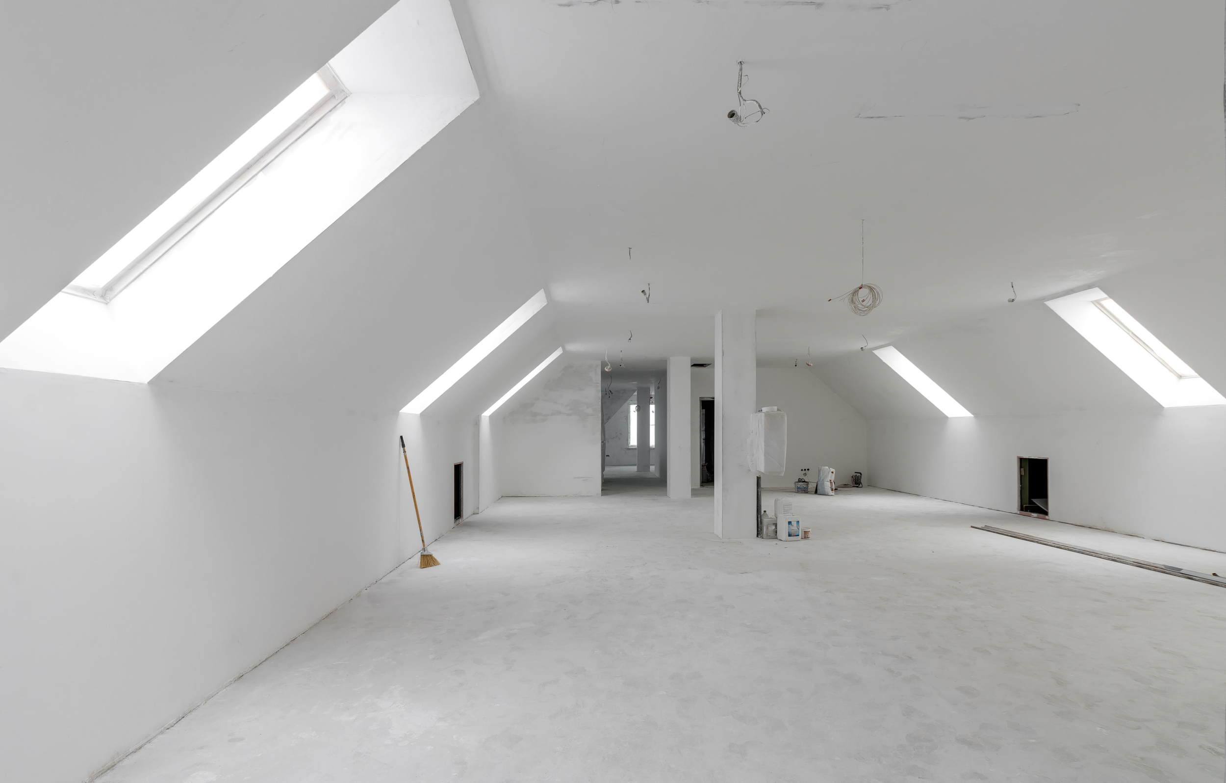 Unfinished attic space with sloped ceilings and skylights, construction materials, and tools scattered around.