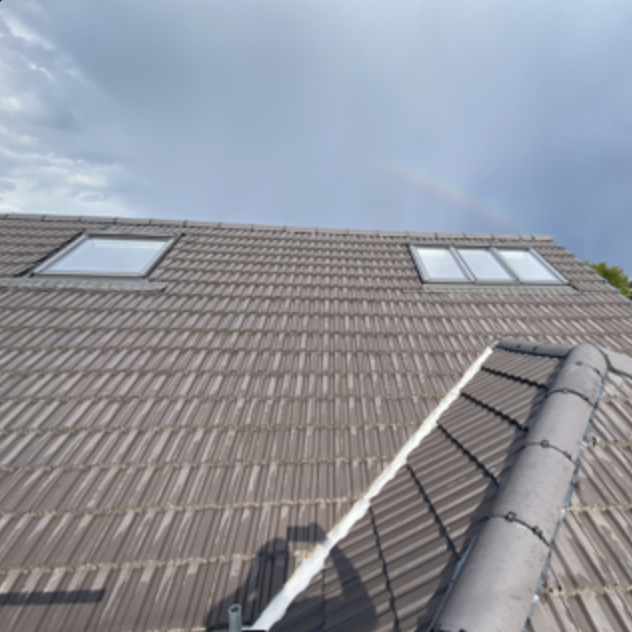 View of a house roof with two skylights, overcast sky, and a faint rainbow in the background.