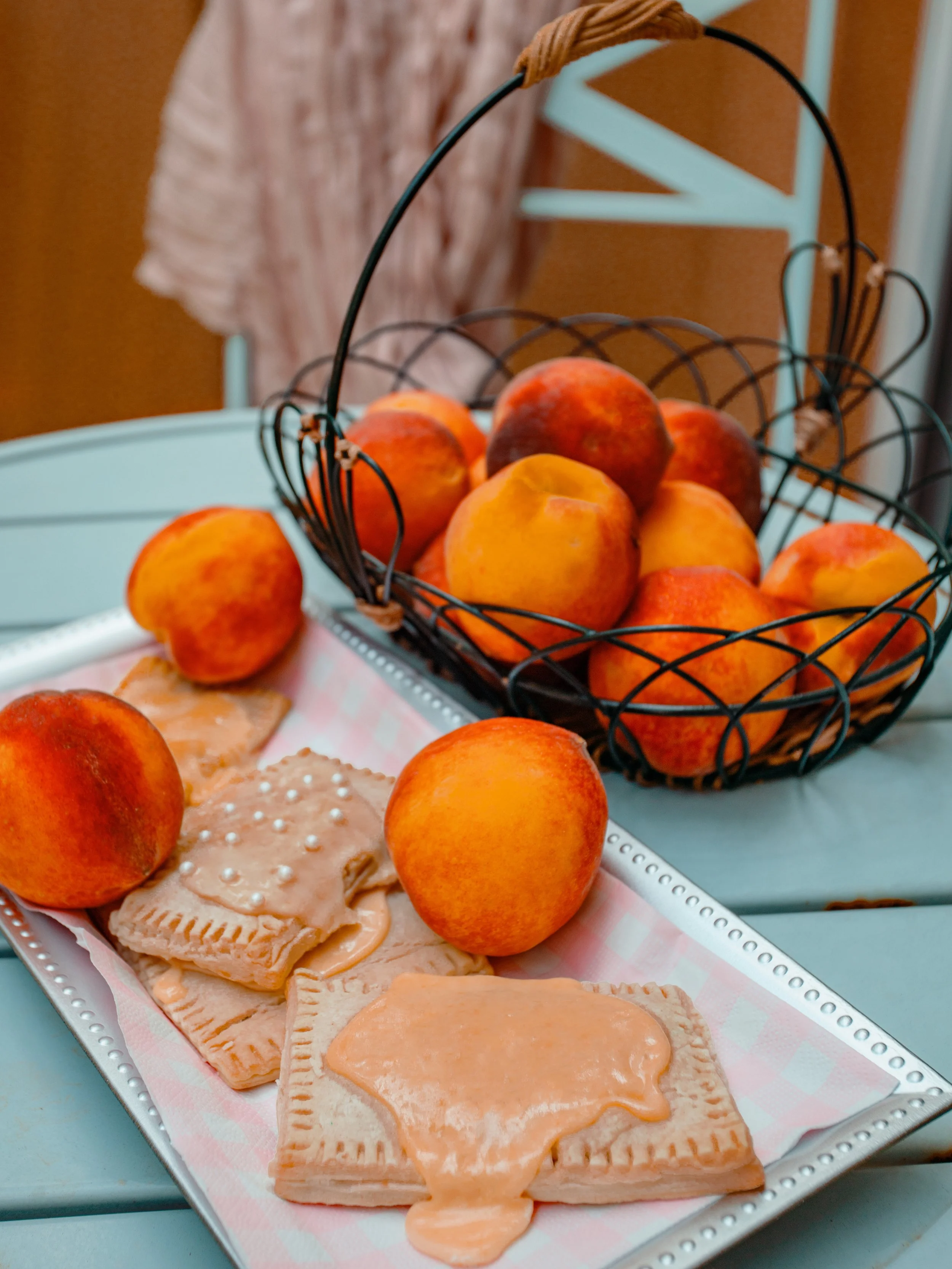 A tray of peach-flavored snacks and fresh peaches in a wire basket on a blue table.