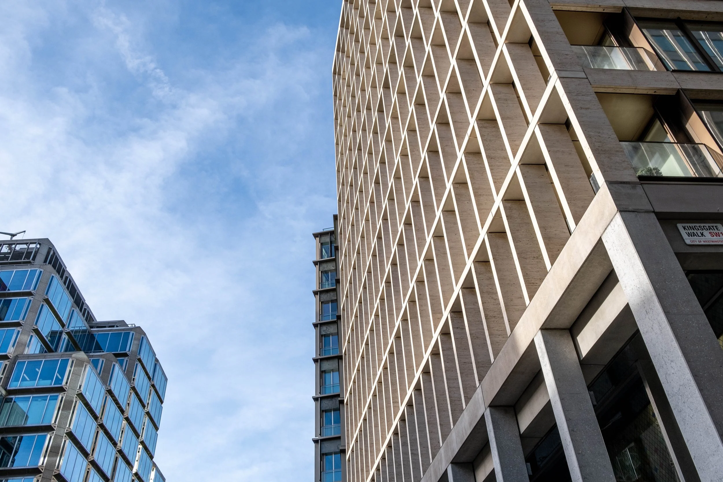 A low-angle view of modern high-rise buildings with glass windows and concrete facades under a blue sky with some clouds.