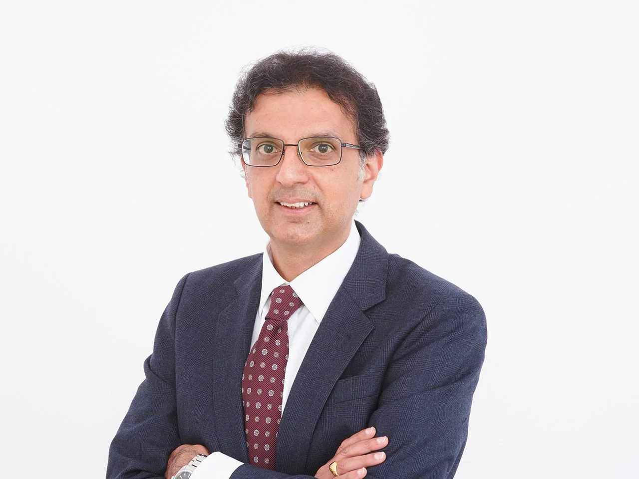 Professional man in a suit with arms crossed, wearing glasses, standing against a white background.