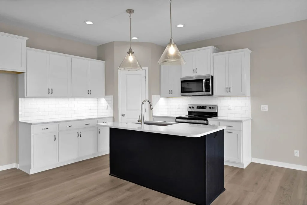 Modern kitchen with white cabinets, black island, stainless steel appliances, pendant lights, and white subway tile backsplash.