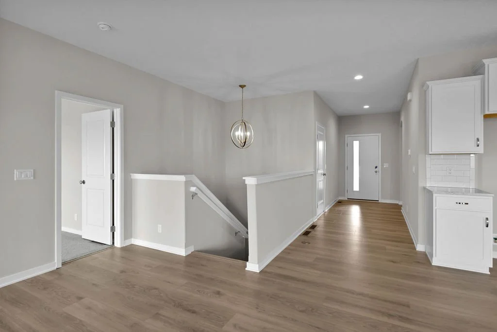 Empty living room with white walls, built-in cabinetry, hardwood floors, and a modern pendant light.