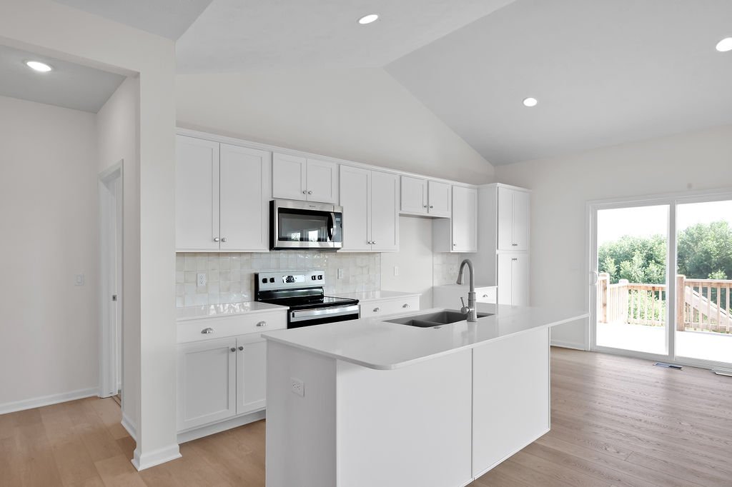 Modern white kitchen with island, stainless steel appliances, and sliding glass door leading to outdoor deck.